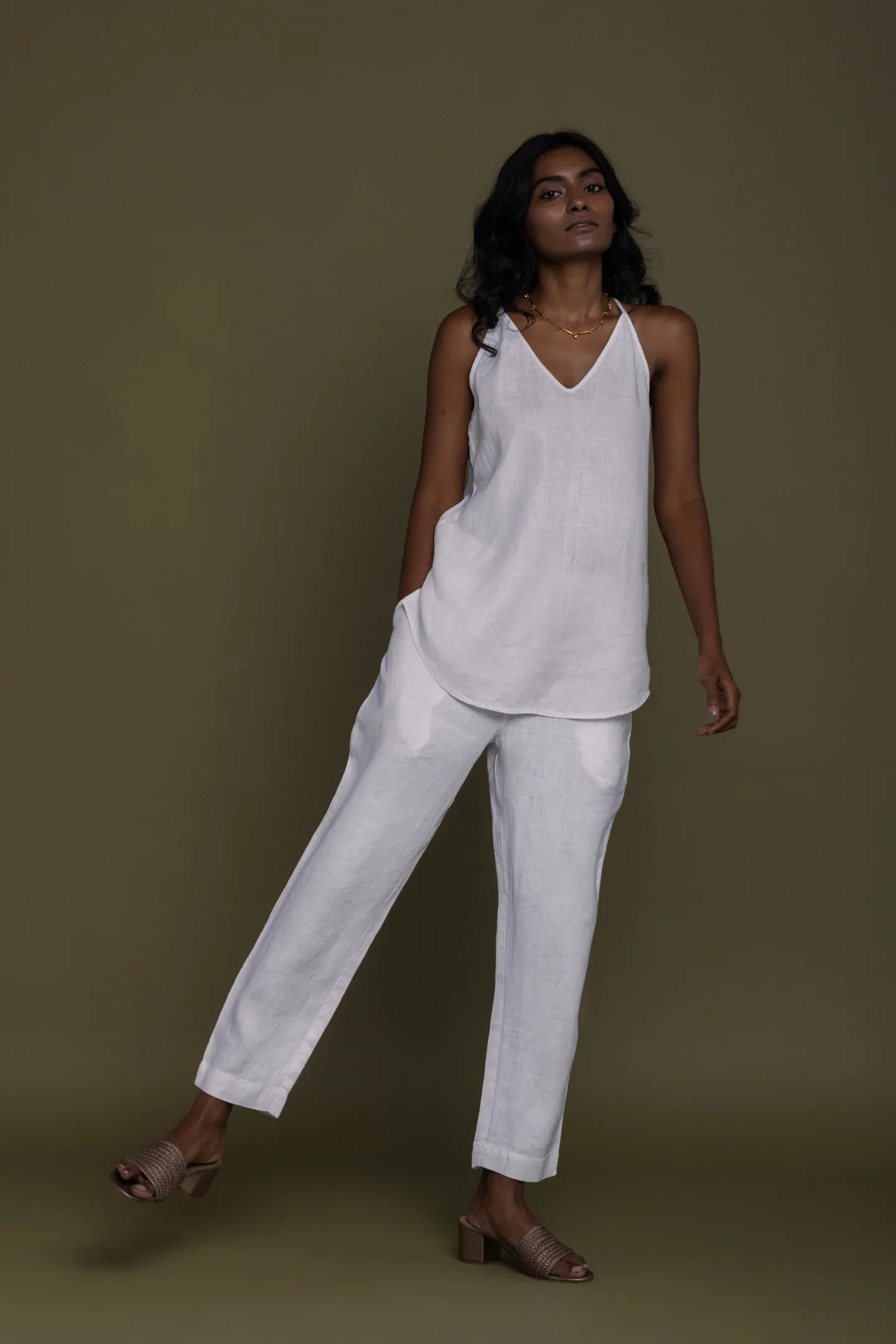 Woman wearing a Reistor white sleeveless top with Blankets on the Beach Pants against a brown background.