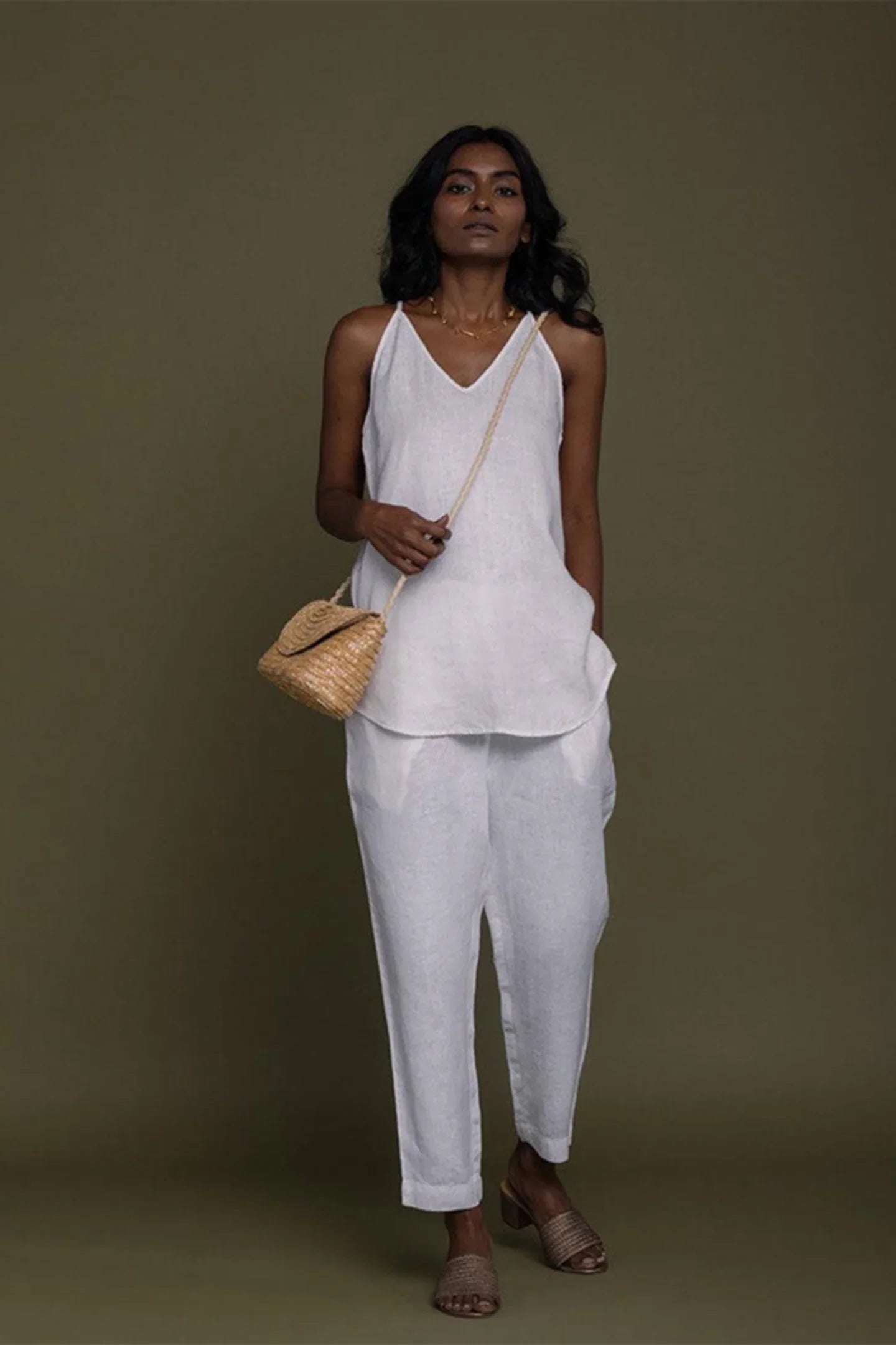 Reistor white sleeveless V-neck top with tapered pants, styled with a woven bag for sustainable women's fashion.