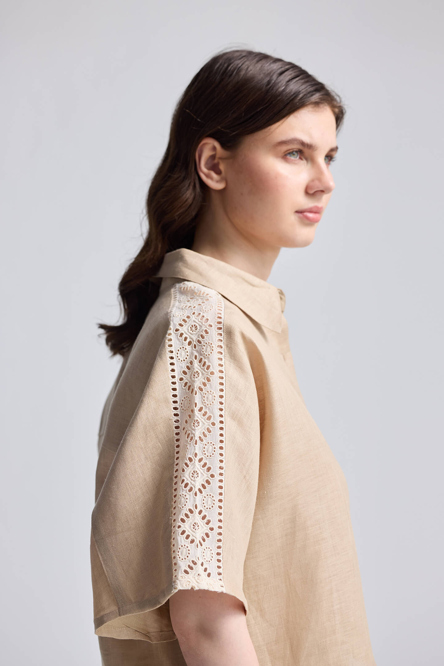 Side profile view of Boxy Shirt with Lace by reistor in beige, featuring a relaxed boxy silhouette and intricate lace detailing along the short sleeves, styled against a neutral background.