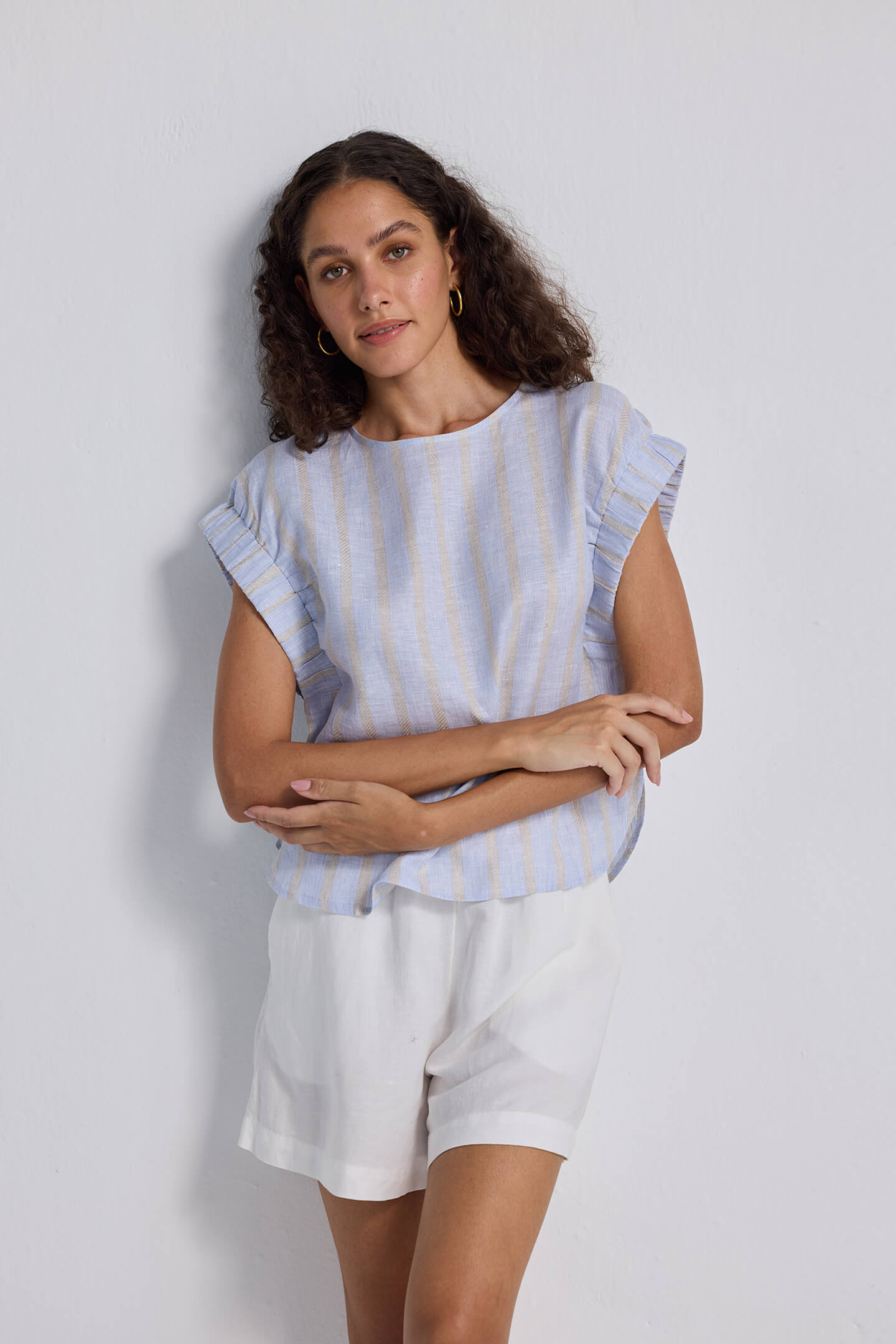 A model showcasing a blue and white striped Boxy Top with Sleeve Detailing by reistor, styled with white linen shorts and black strappy sandals for a summer look.