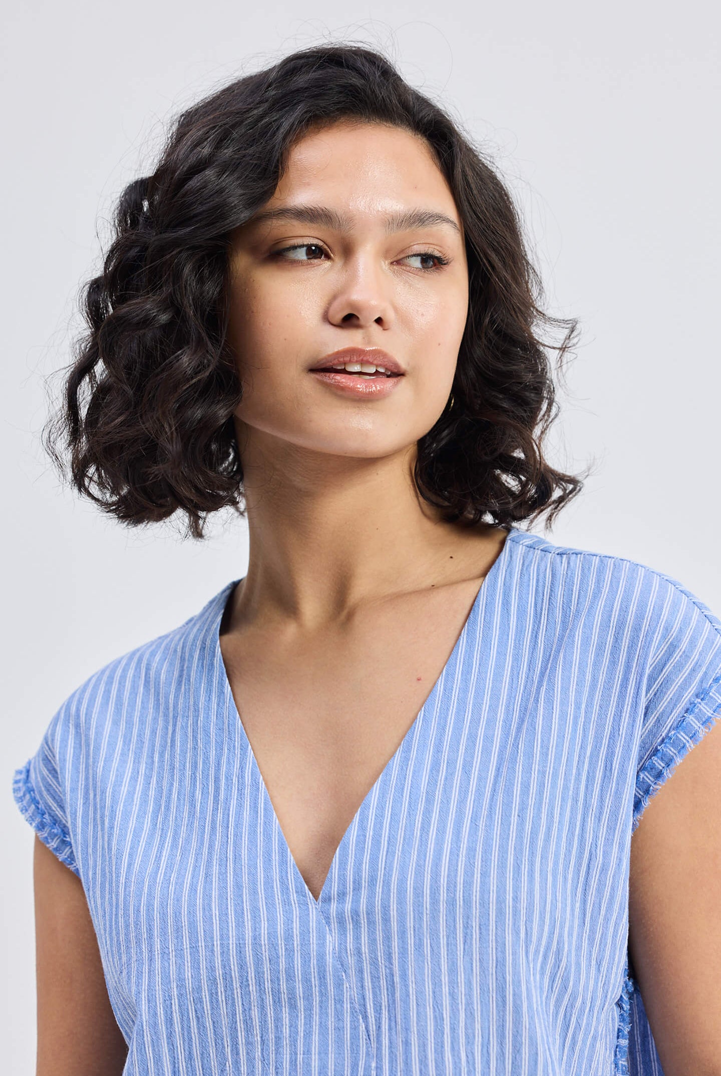 Model wearing the Reistor Boxy V-neck Top with Fray Detail, a blue and white striped sustainable women's top with frayed sleeve edges.
