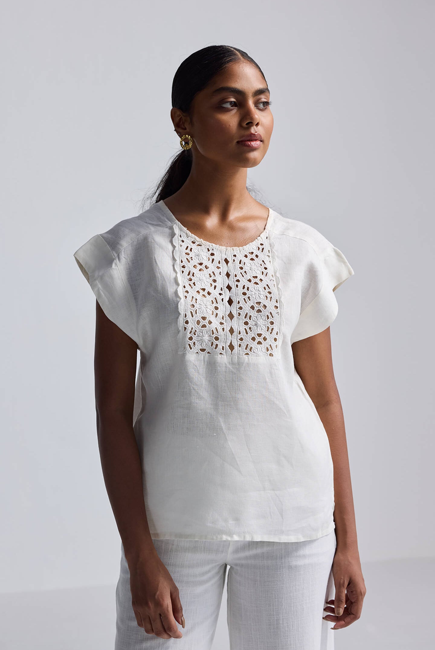 A woman styled in a neutral beige reistor Boxy shirt with Embroidered Lace Detail, highlighting its relaxed silhouette and summer-ready hemp fabric.
