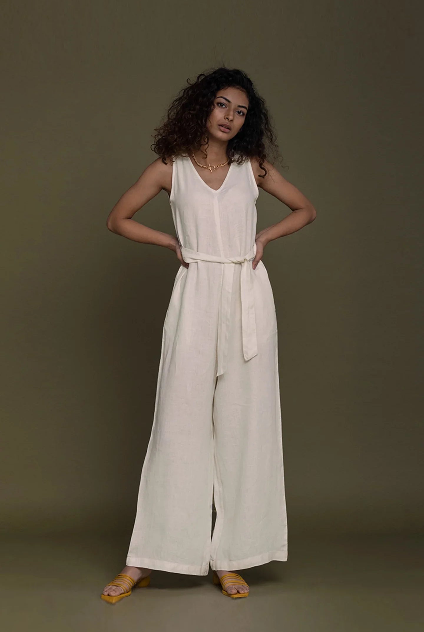 Woman wearing a Reistor white sleeveless jumpsuit against a brown background.