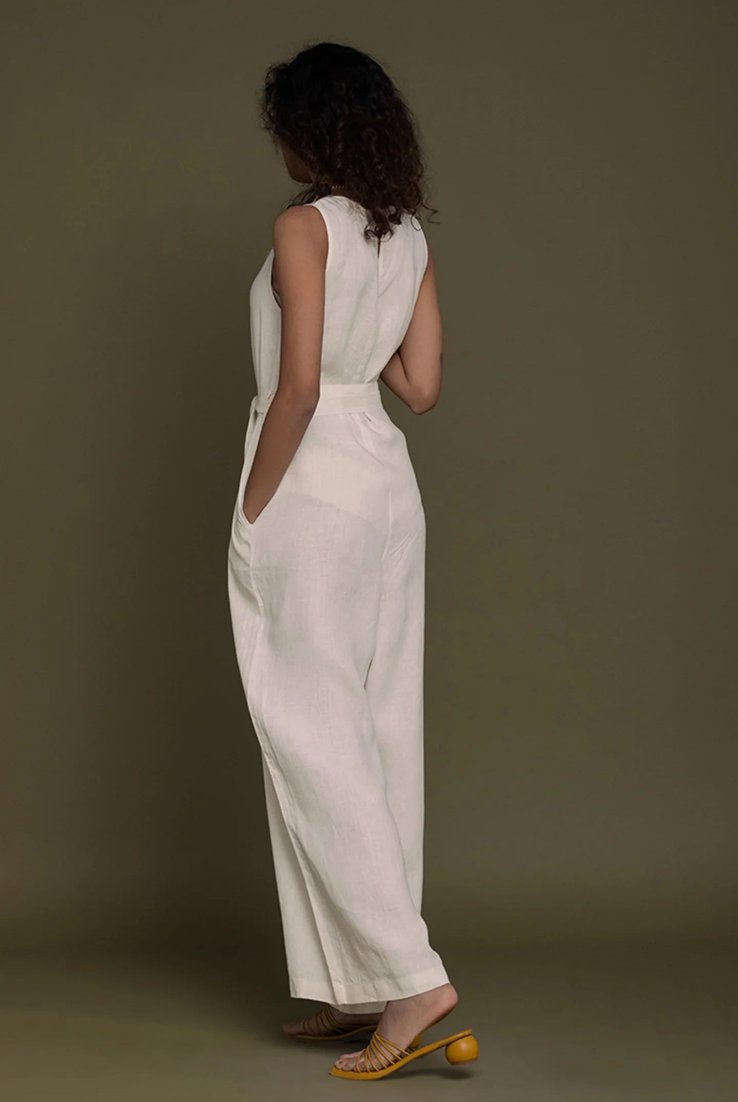 Woman wearing a Reistor white sleeveless top and wide-leg pants against a brown background.