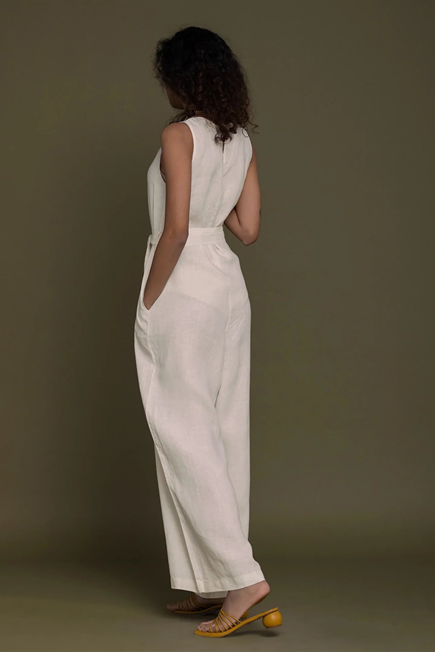 Woman wearing a Reistor white sleeveless top and wide-leg pants against a brown background.