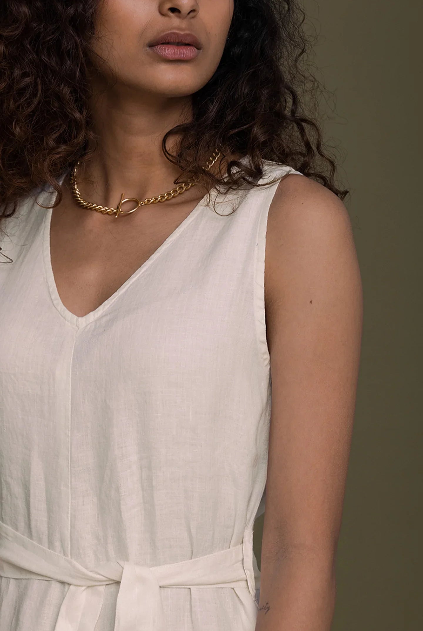 Close-up of Reistor sleeveless V-neck beige jumpsuit with tie waist, crafted for timeless sustainable women's fashion.