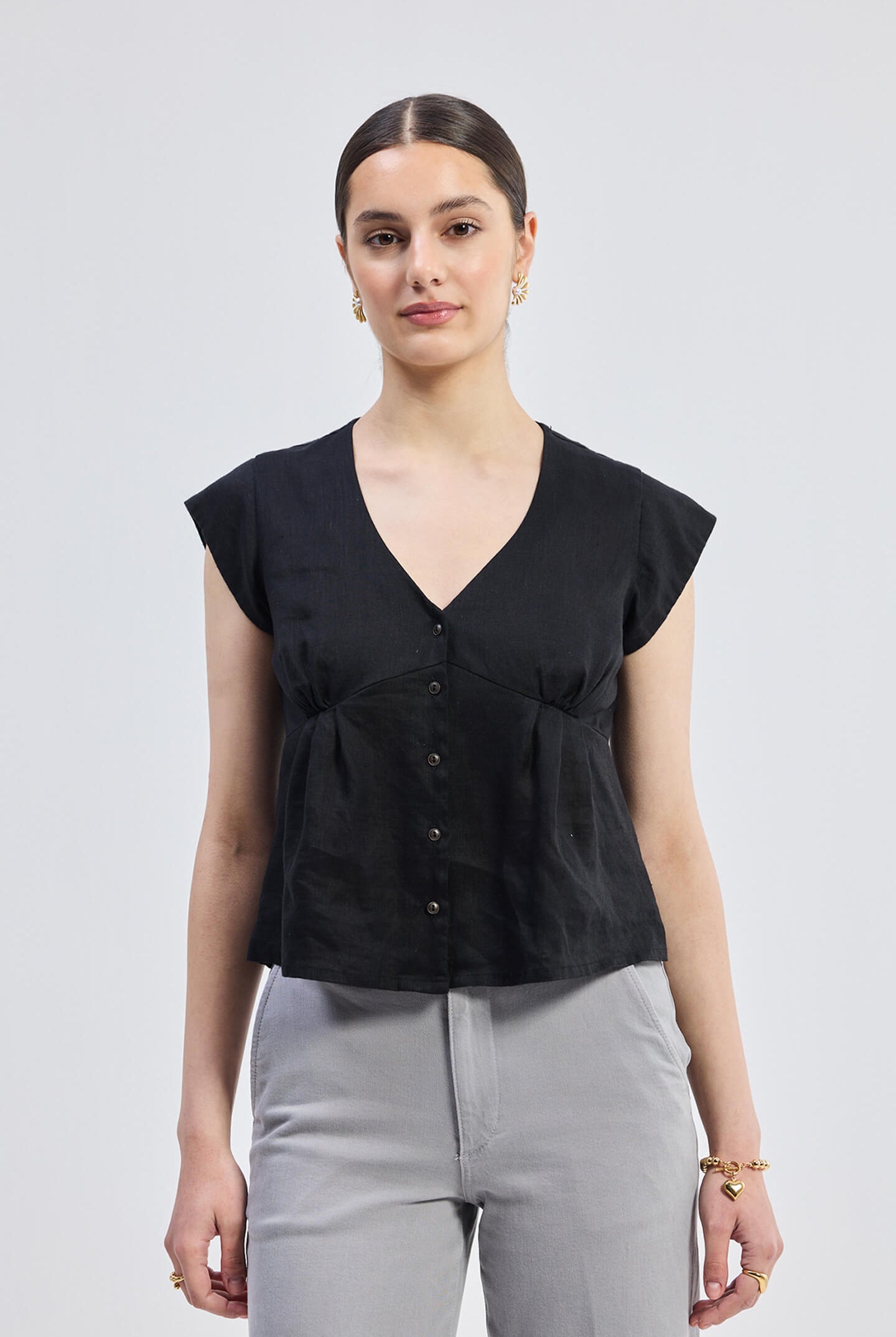 A woman wearing a black deep V-neck short top with cap sleeves and buttons at the front.