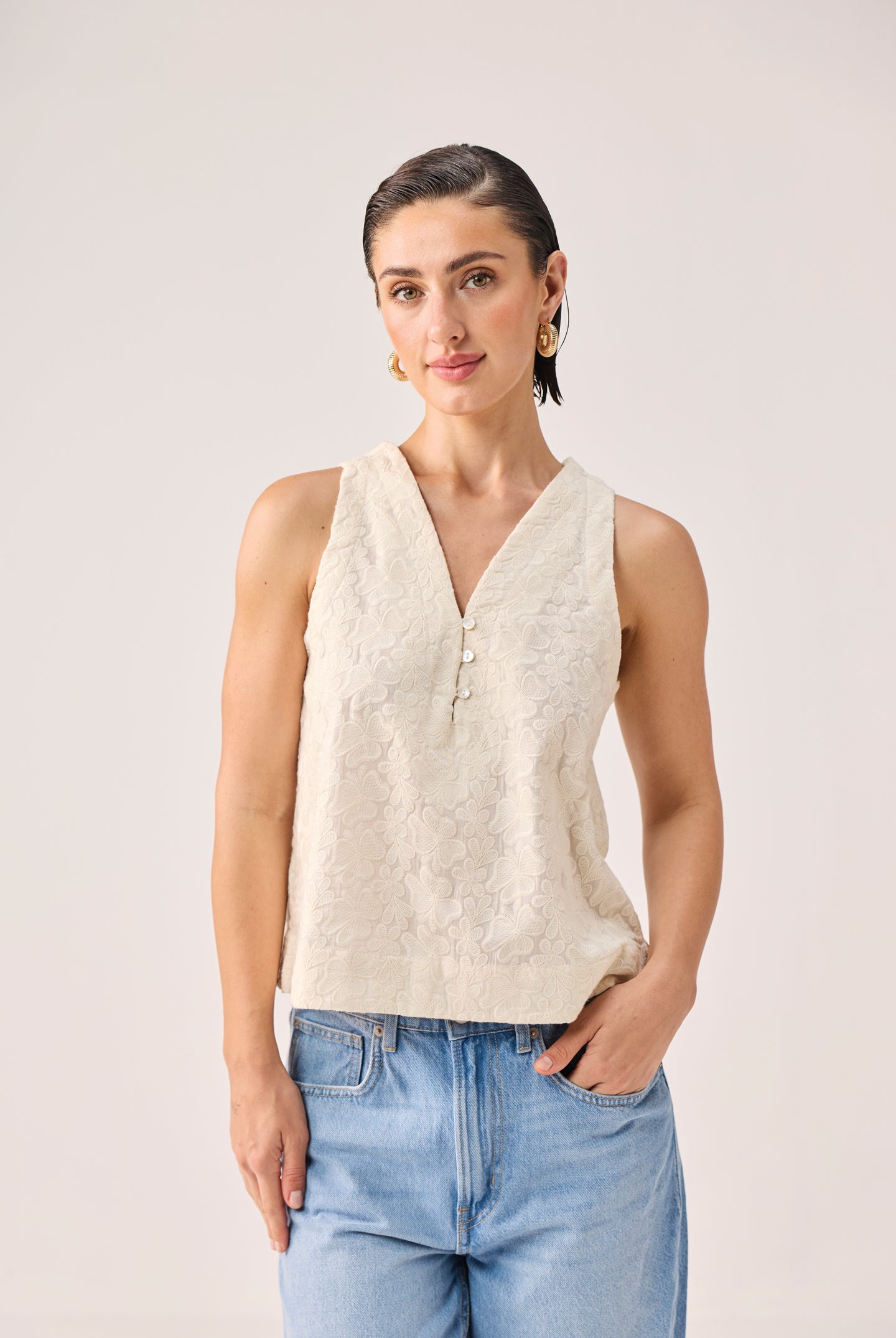 Woman wearing a beige sleeveless top and blue jeans against a plain background