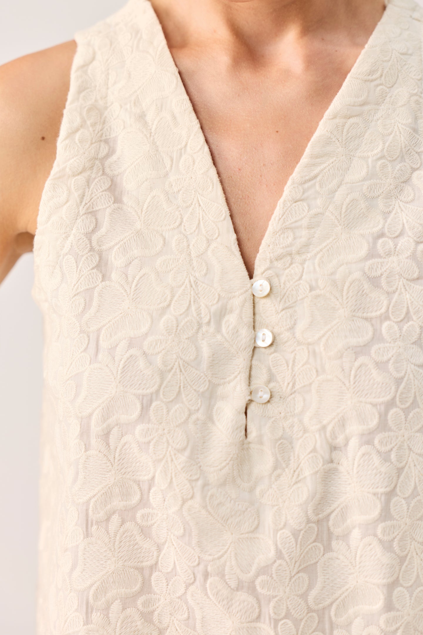 Close-up of a beige textured sleeveless top with buttons on a white background