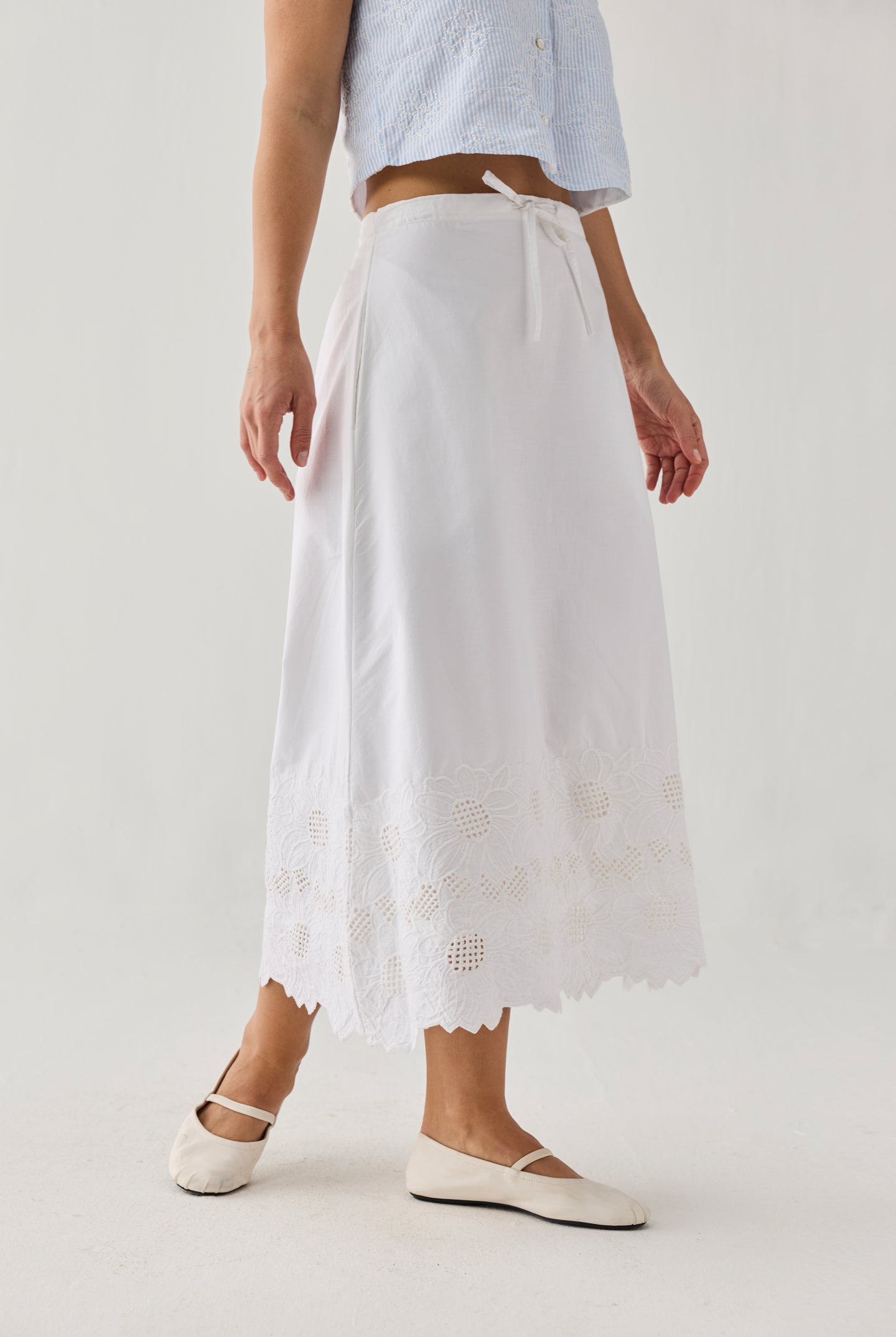 Person wearing a light blue top and white skirt with lace details on a plain background