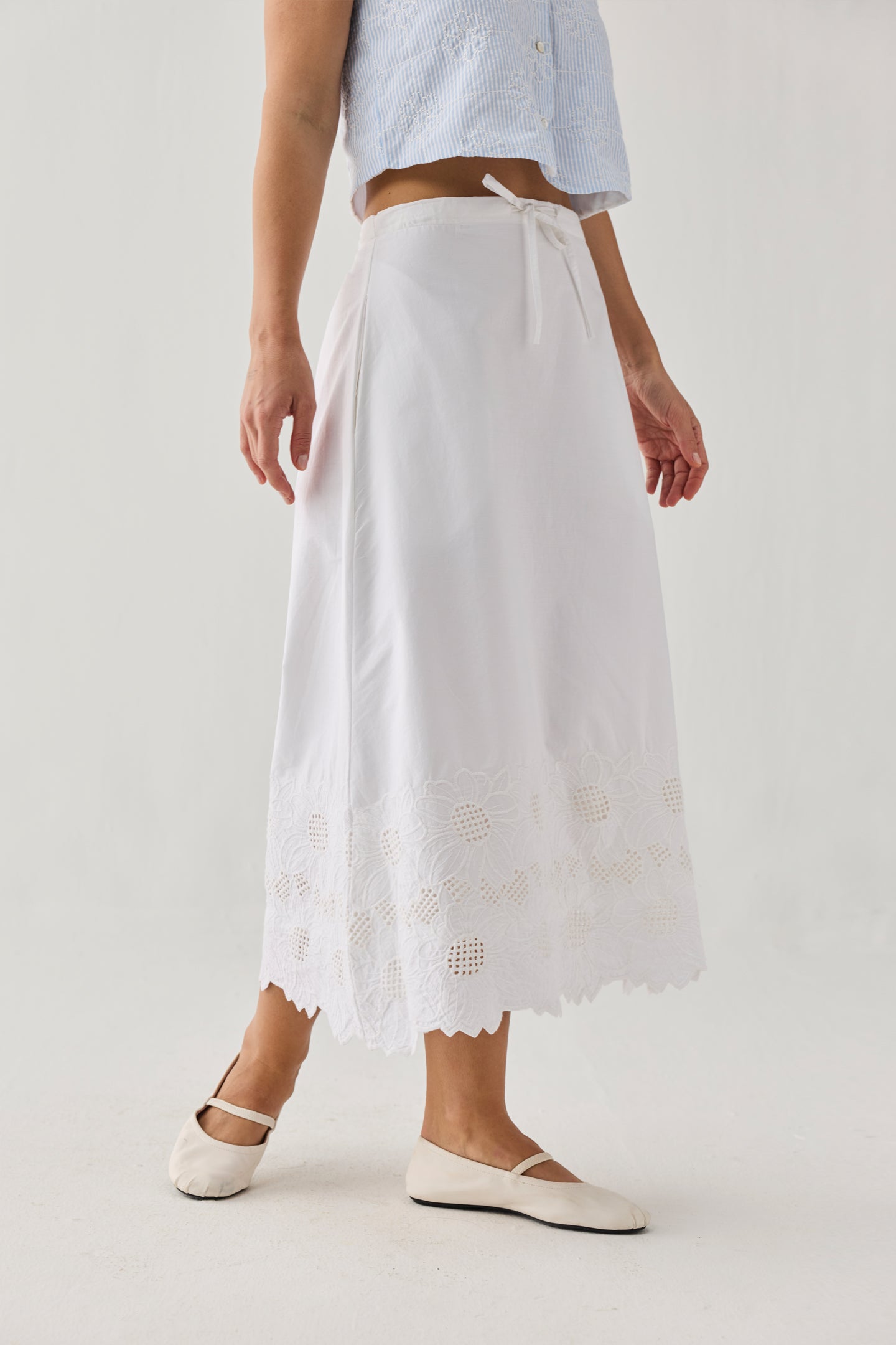 Person wearing a light blue top and white skirt with lace details on a plain background