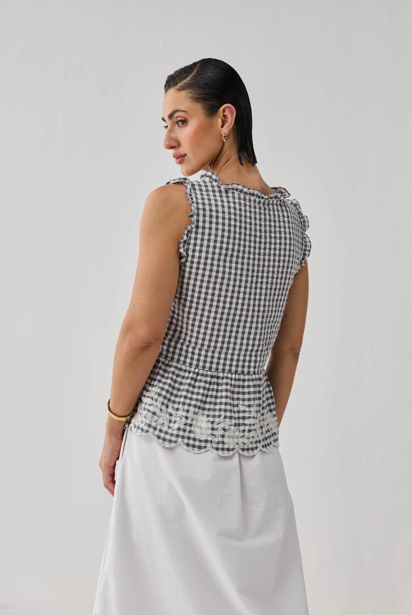 Woman wearing a black and white checkered top with ruffled details on a plain background