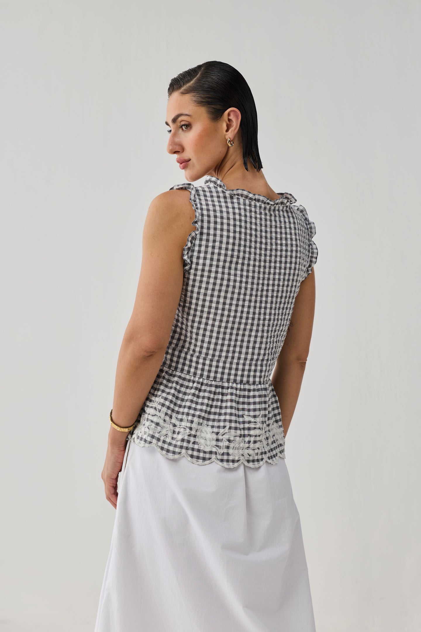 Woman wearing a black and white checkered top with ruffled details on a plain background