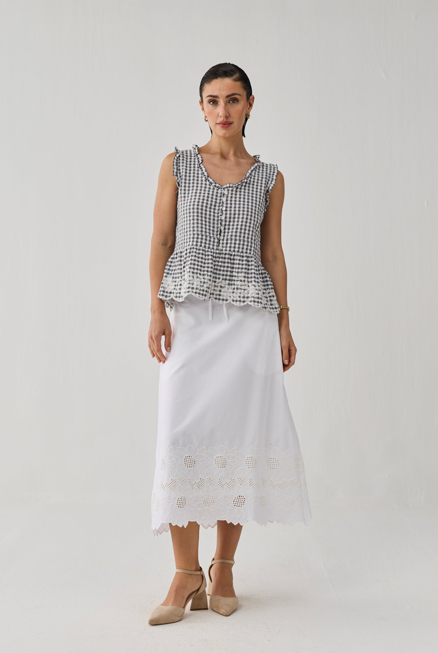 Woman wearing a black and white checkered top with a peplum waist and a white skirt with embroidery on a plain background