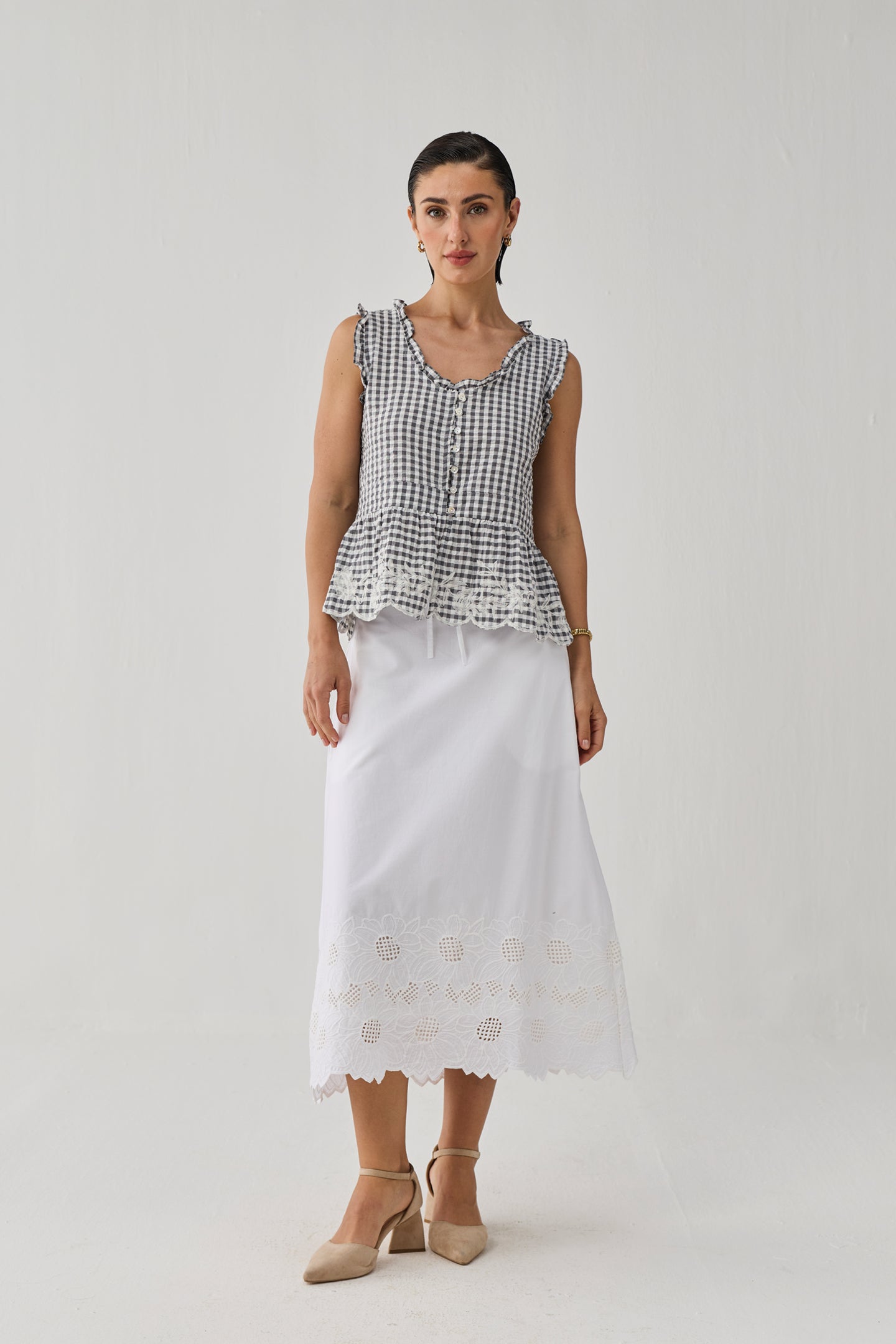 Woman wearing a black and white checkered top with a peplum waist and a white skirt with embroidery on a plain background
