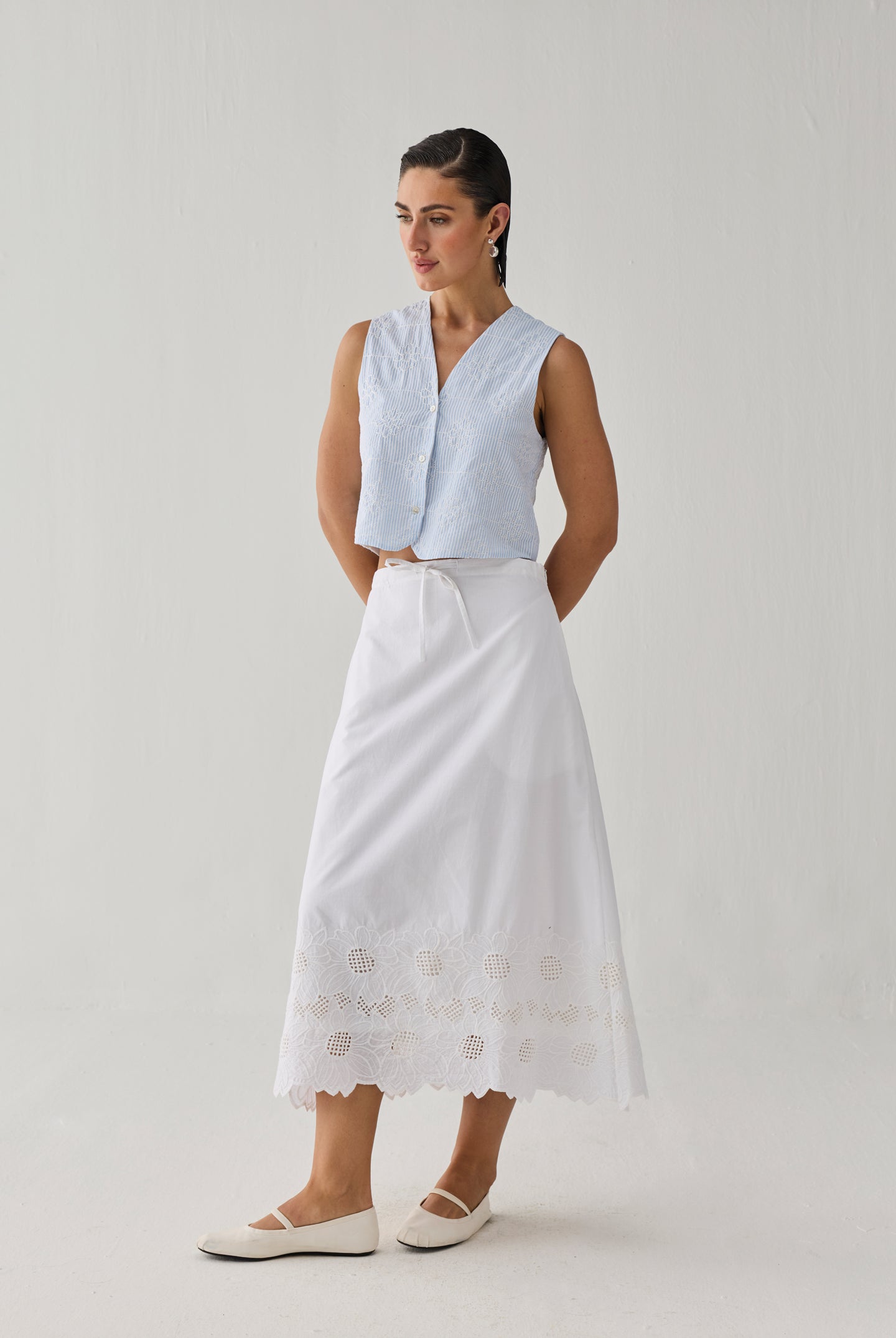 Embroidered Sleeveless Vest Top in Blue Stripe featuring delicate tonal embroidery, a textured striped pattern, V-neckline, and button-front closure, styled with a white embroidered midi skirt and shown in a full-length studio setting.
