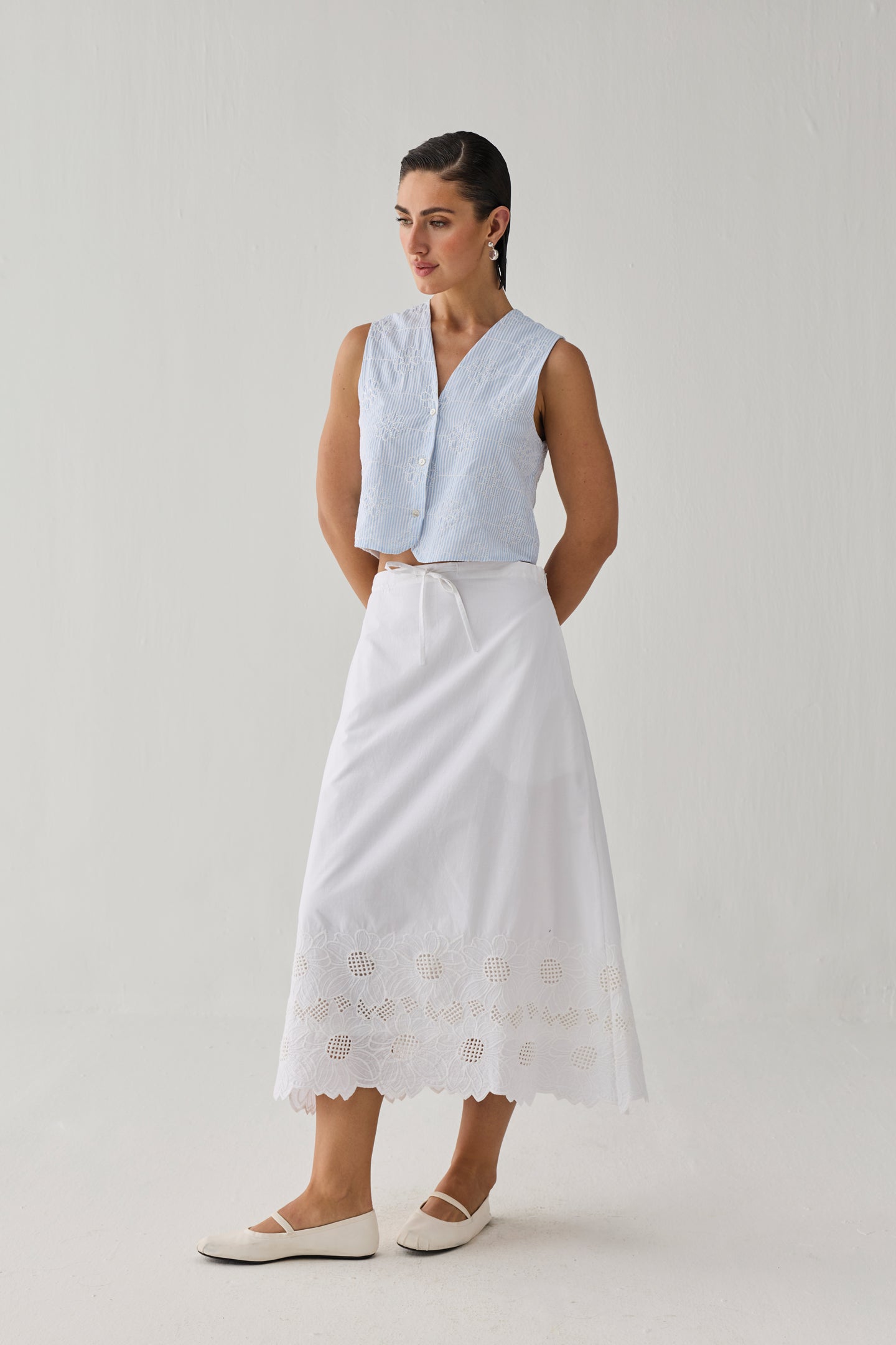 Embroidered Sleeveless Vest Top in Blue Stripe featuring delicate tonal embroidery, a textured striped pattern, V-neckline, and button-front closure, styled with a white embroidered midi skirt and shown in a full-length studio setting.