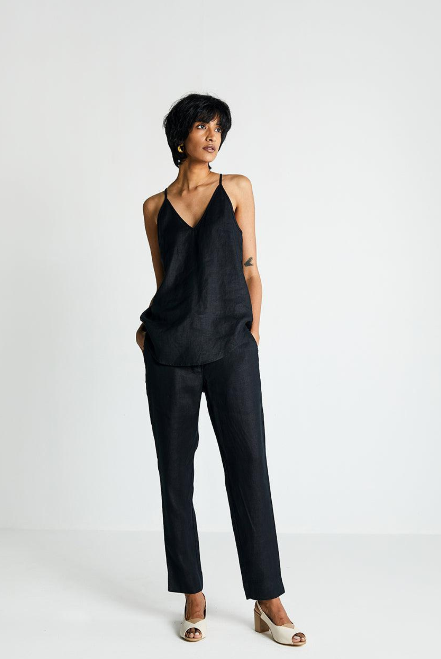 Woman wearing Reistor Endless Sunday Top in Black with matching black pants on a white background, sleeveless sustainable top with a relaxed fit for everyday style.