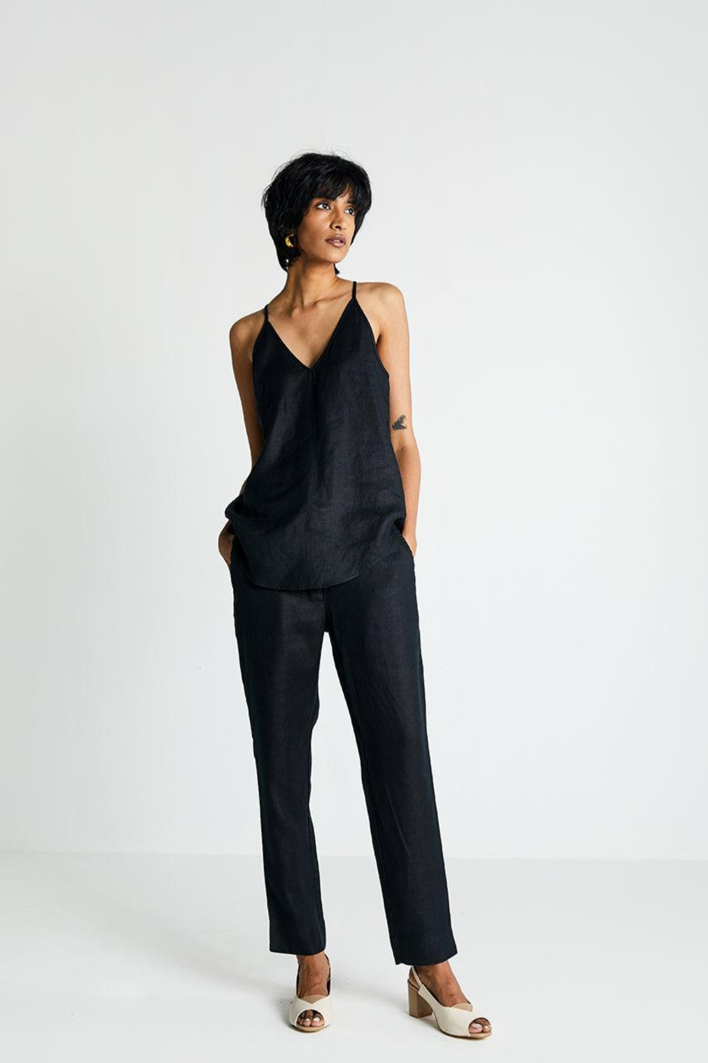 Woman wearing Reistor Endless Sunday Top in Black with matching black pants on a white background, sleeveless sustainable top with a relaxed fit for everyday style.
