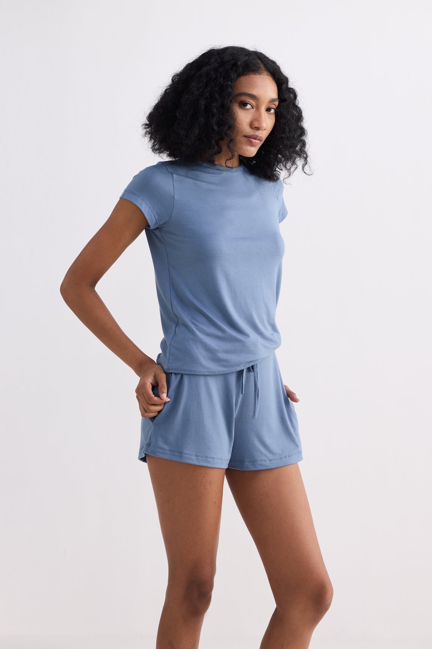 A full-length studio shot of a model wearing the reistor Essential Short Sleeve Tee Set in Blue, showcasing the relaxed fit of the sustainable short-sleeved top and matching drawstring shorts for a casual, eco-friendly summer look.