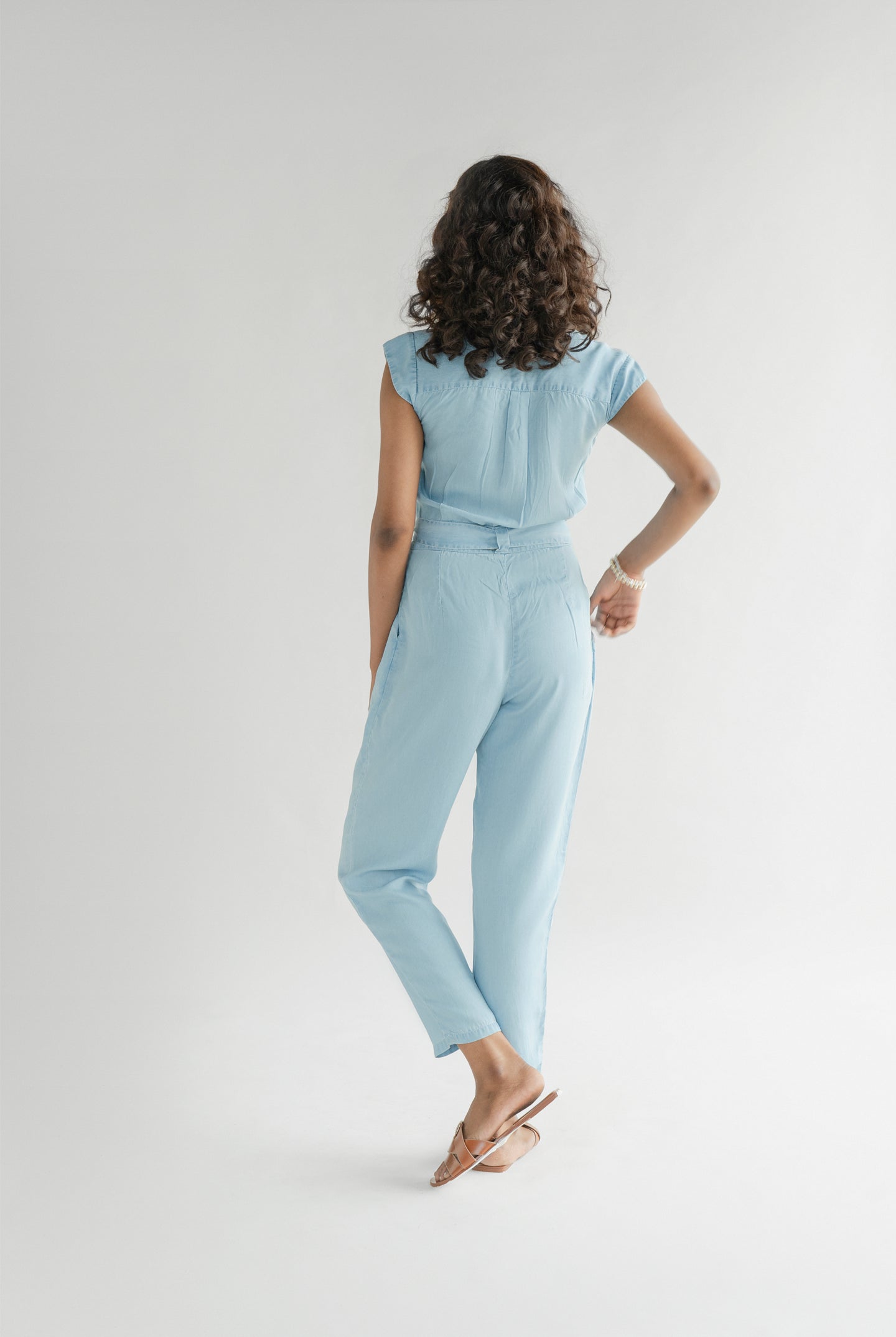 Back view of Reistor Evening Chai Jumpsuit in Blue Denim featuring a relaxed fit, cap sleeves, tapered legs, and a breathable sustainable design for everyday wear.