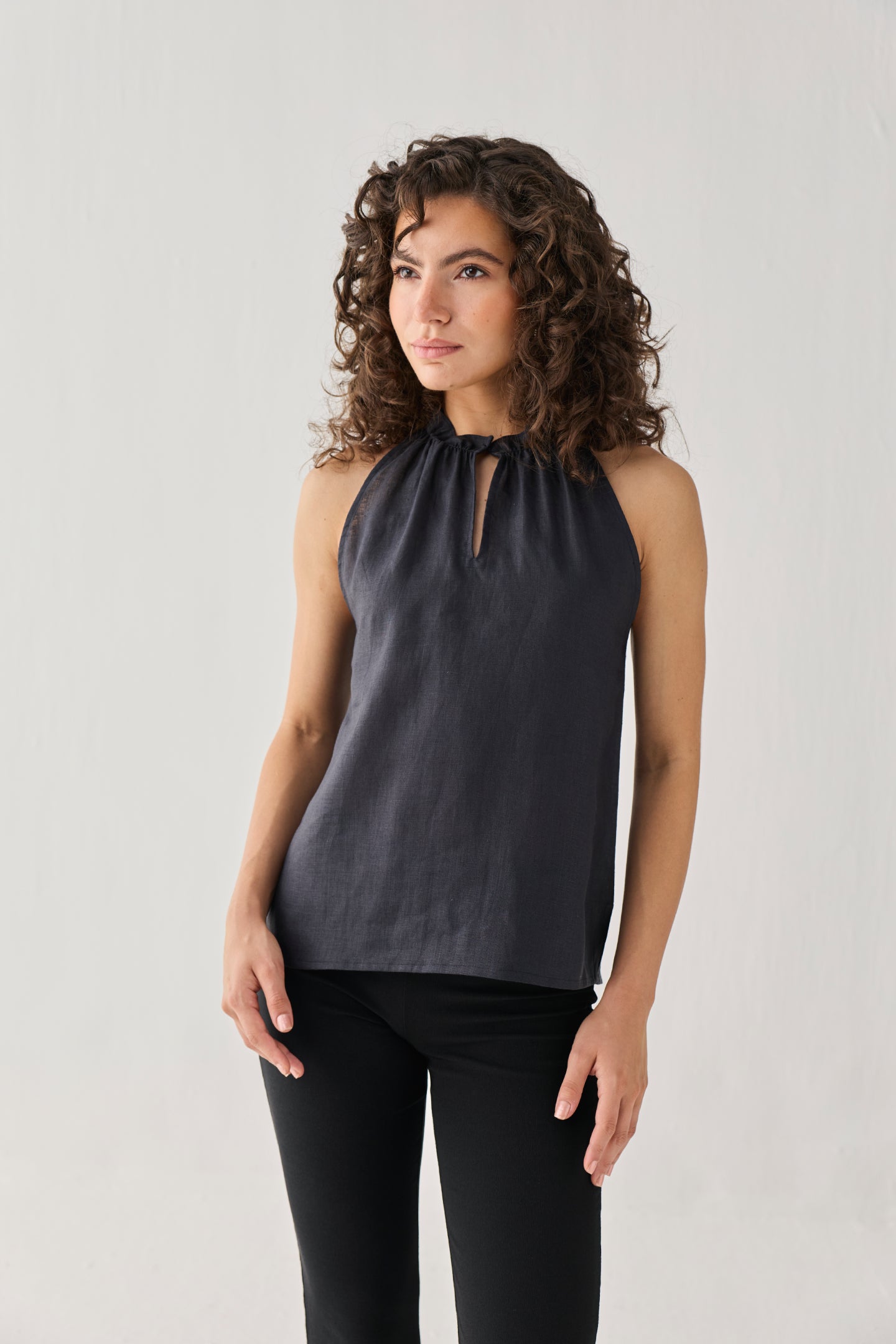 Woman wearing a dark gray sleeveless top with a cutout neckline against a light background