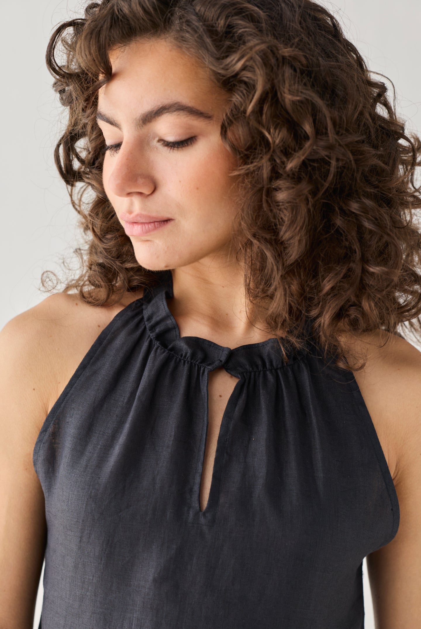 Reistor Halter Neck Top in Black featuring an elegant keyhole opening and softly ruched neckline, captured in a close-up portrait that highlights its refined craftsmanship and timeless appeal.