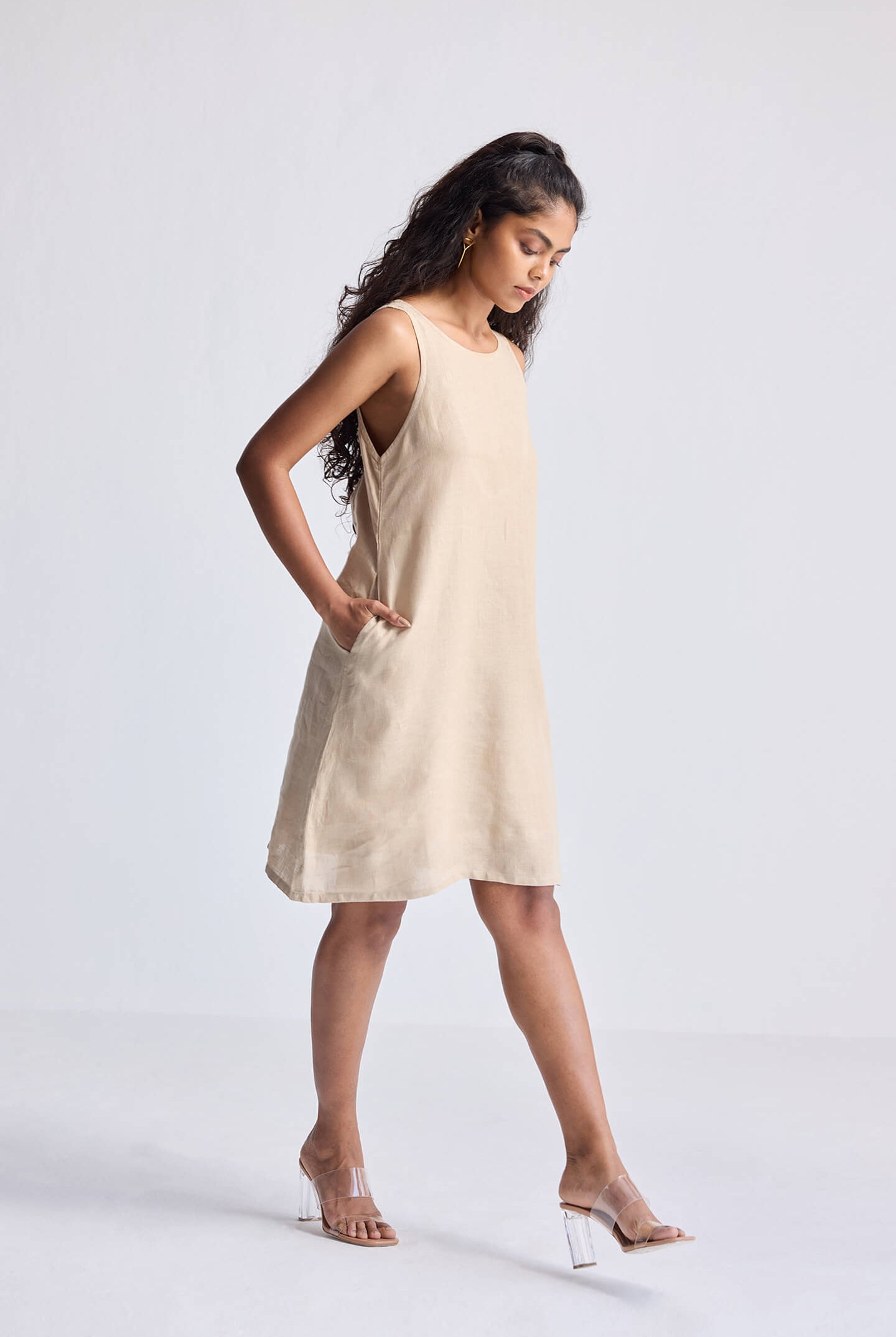 Model wearing the reistor Hemp Short Dress with Back Embroidered Lace Detail in natural beige hemp fabric, sleeveless A-line silhouette with side pockets, styled for a minimal sustainable fashion look.