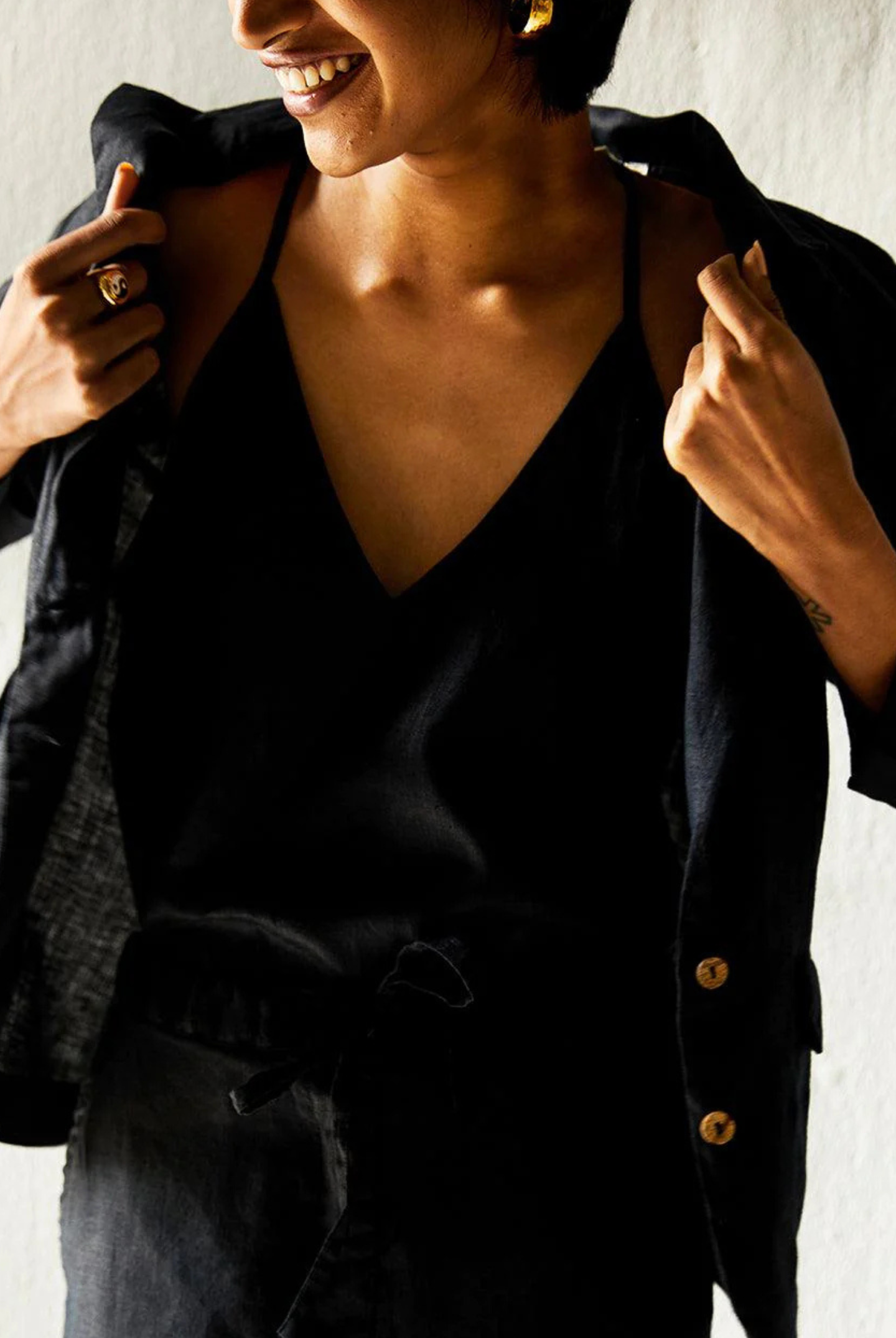 Person wearing a black outfit with a deep neckline and buttons, smiling.