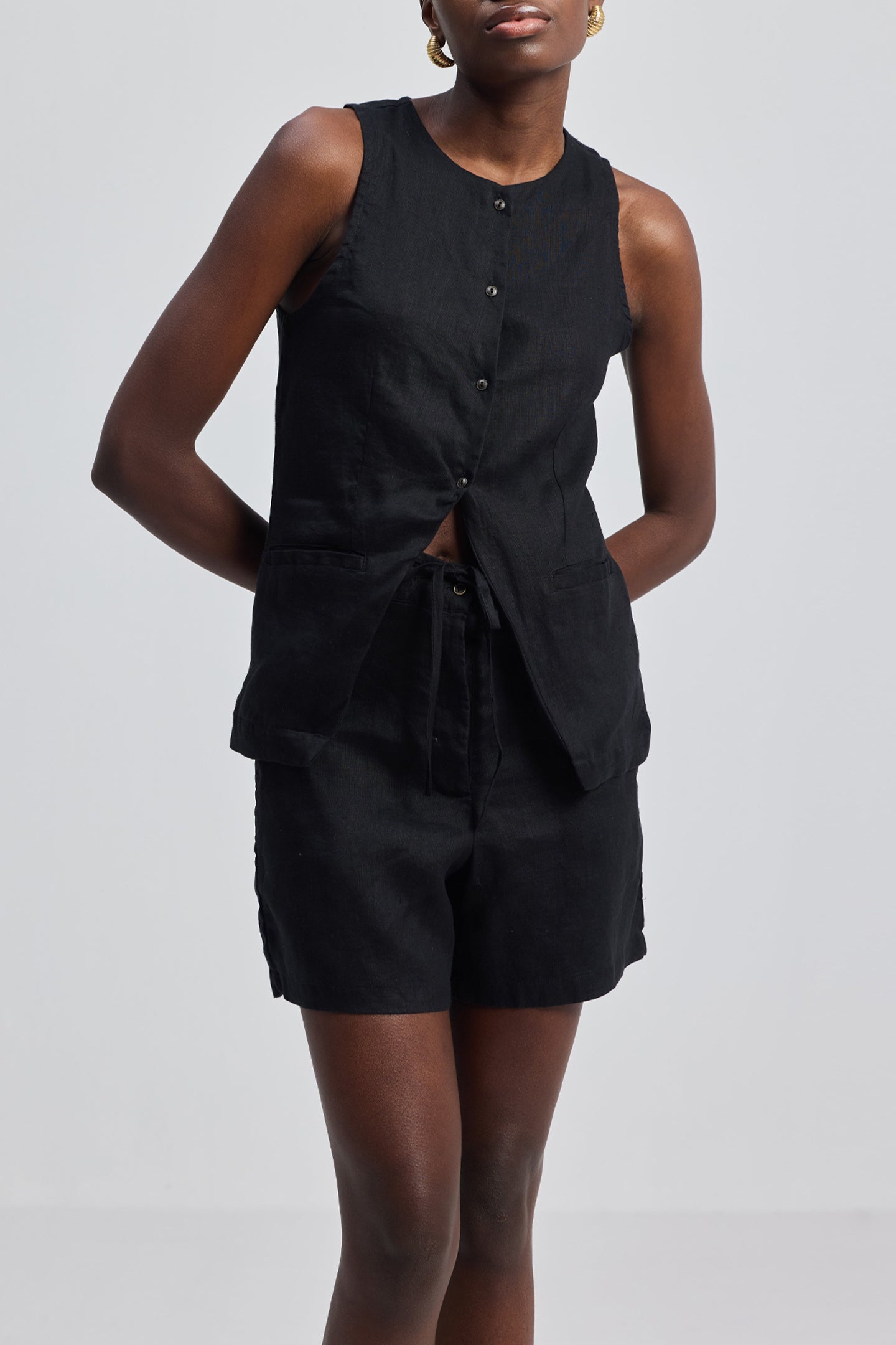 A person wearing a black hemp vest jacket set with front button closure and pockets, paired with matching shorts.
