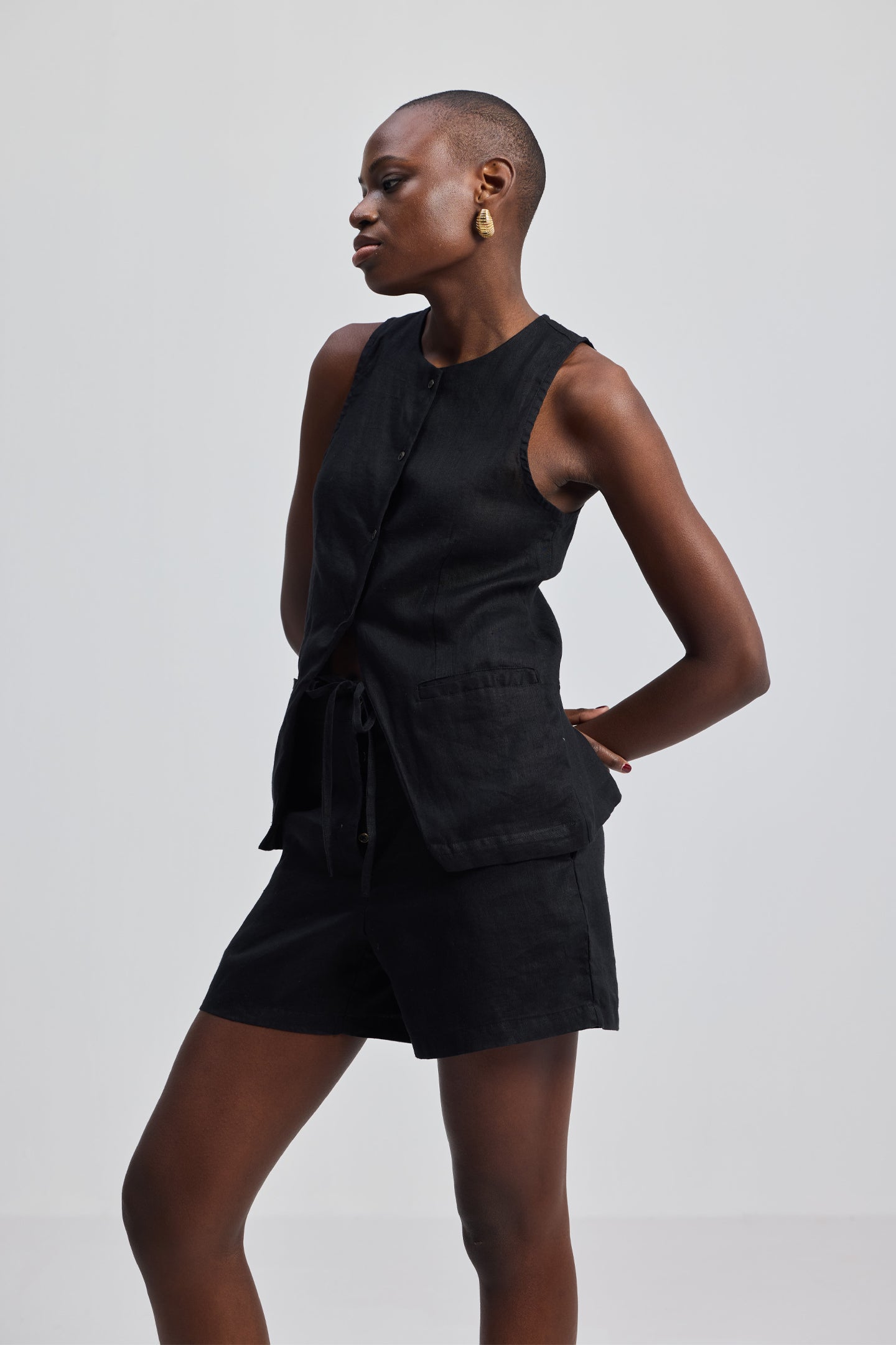 Side profile of a model wearing the reistor Hemp Vest Jacket Set in Black, featuring a tailored sleeveless vest and matching high-waisted shorts made from sustainable hemp fabric.