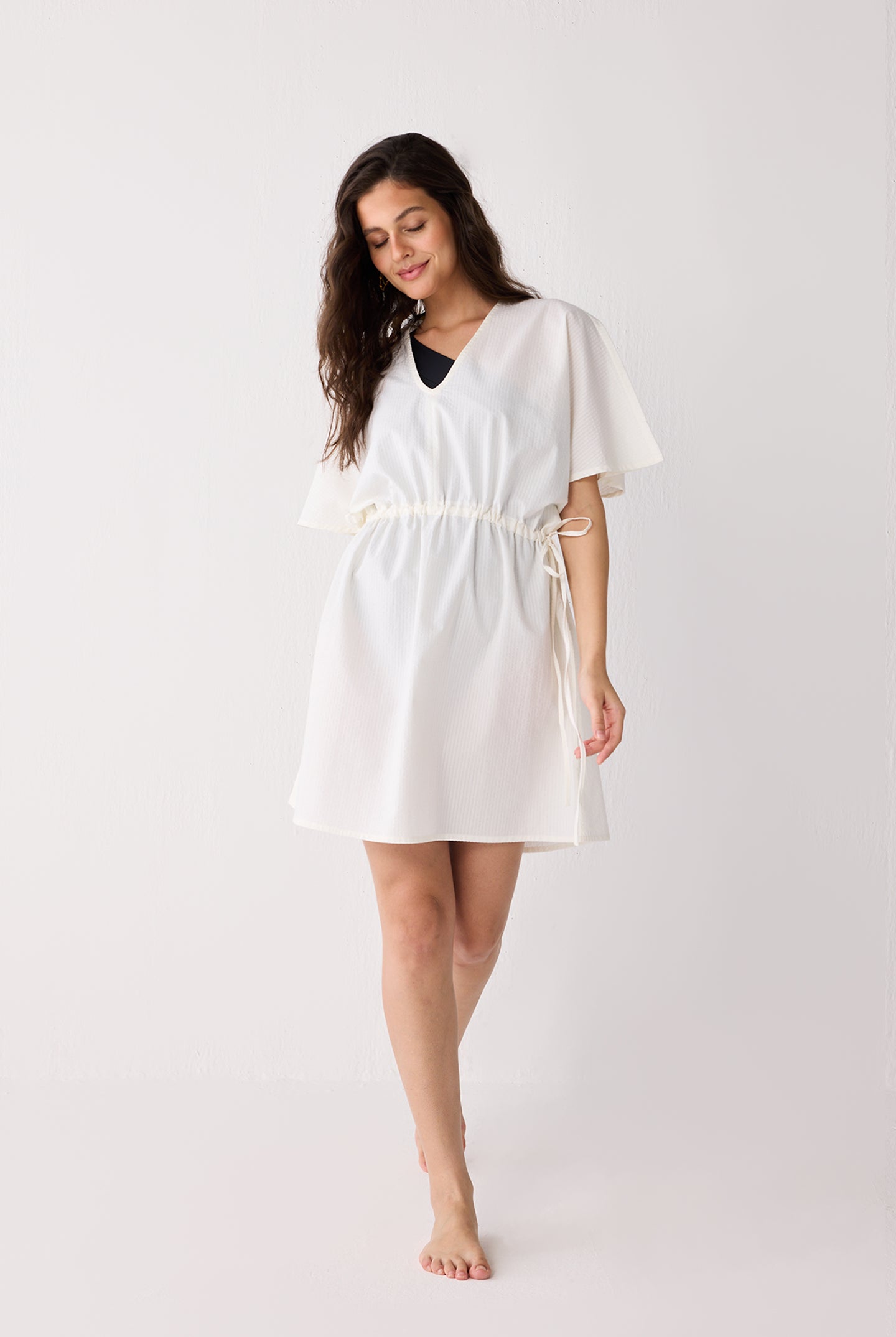 Woman wearing a white dress with a belt on a plain background