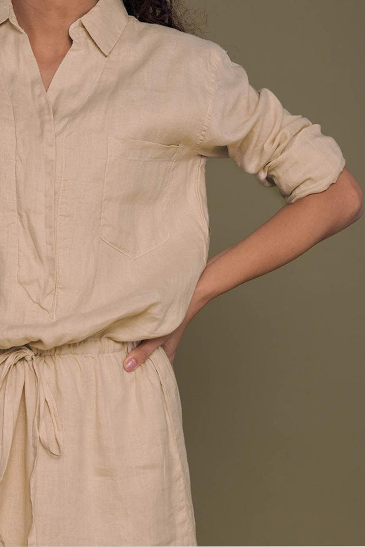 Person wearing the Meet me by the Cliff Dress in Neutral Beige by Reistor with rolled-up sleeves against a brown background