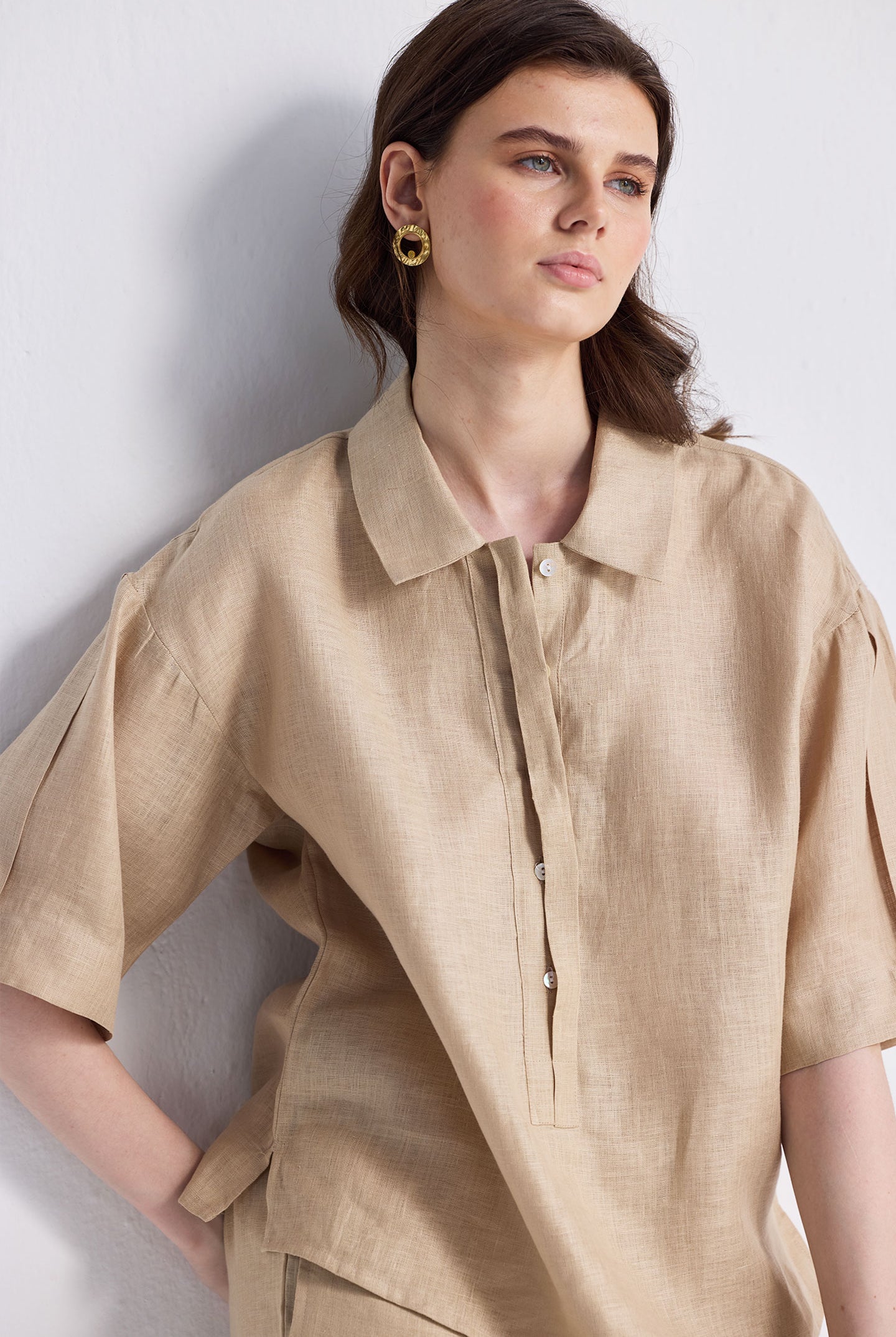 Woman modeling the Reistor Oversized Flowy Shirt in Neutral Beige, a relaxed-fit linen button-up with short sleeves and a classic collar, paired with matching pants on a white background.
