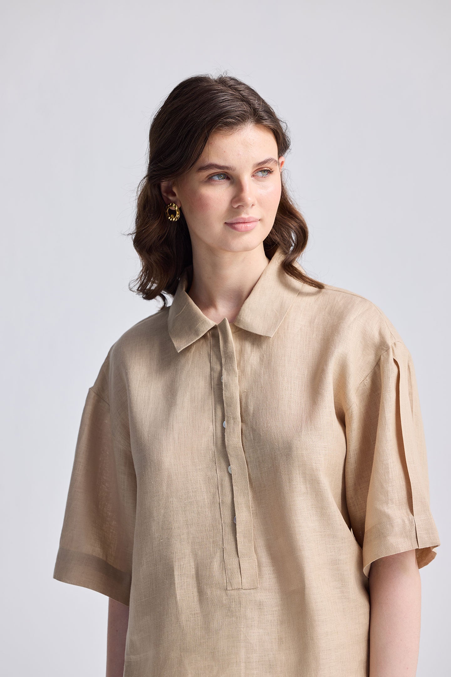 Model wearing the Reistor Oversized Flowy Shirt in Neutral Beige, a relaxed-fit linen button-up with short sleeves and a classic collar, styled with matching beige pants on a white background.