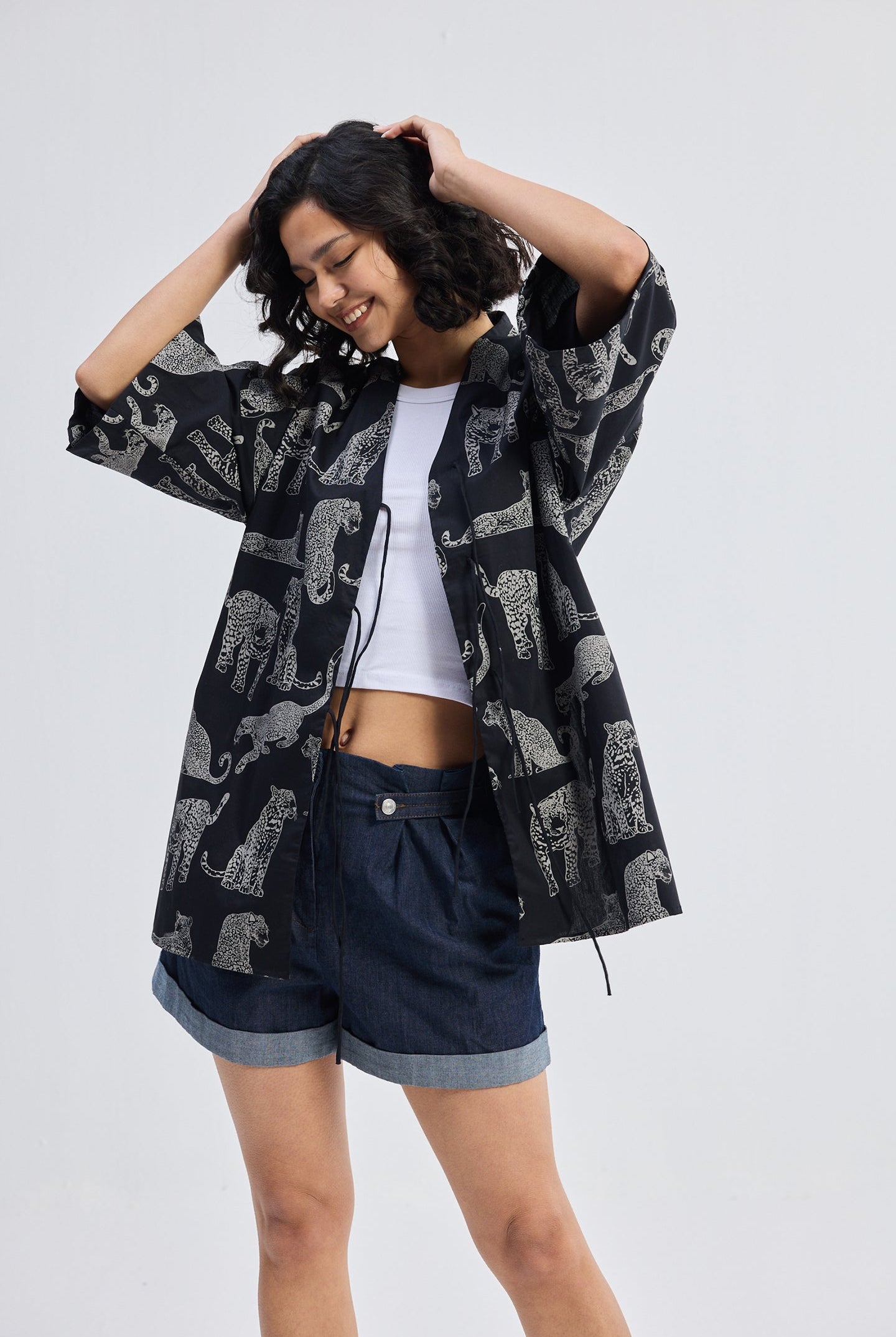 Woman wearing Oversized Shirt with Front-ties in Animal Print by reistor, paired with denim shorts on a clean white background.