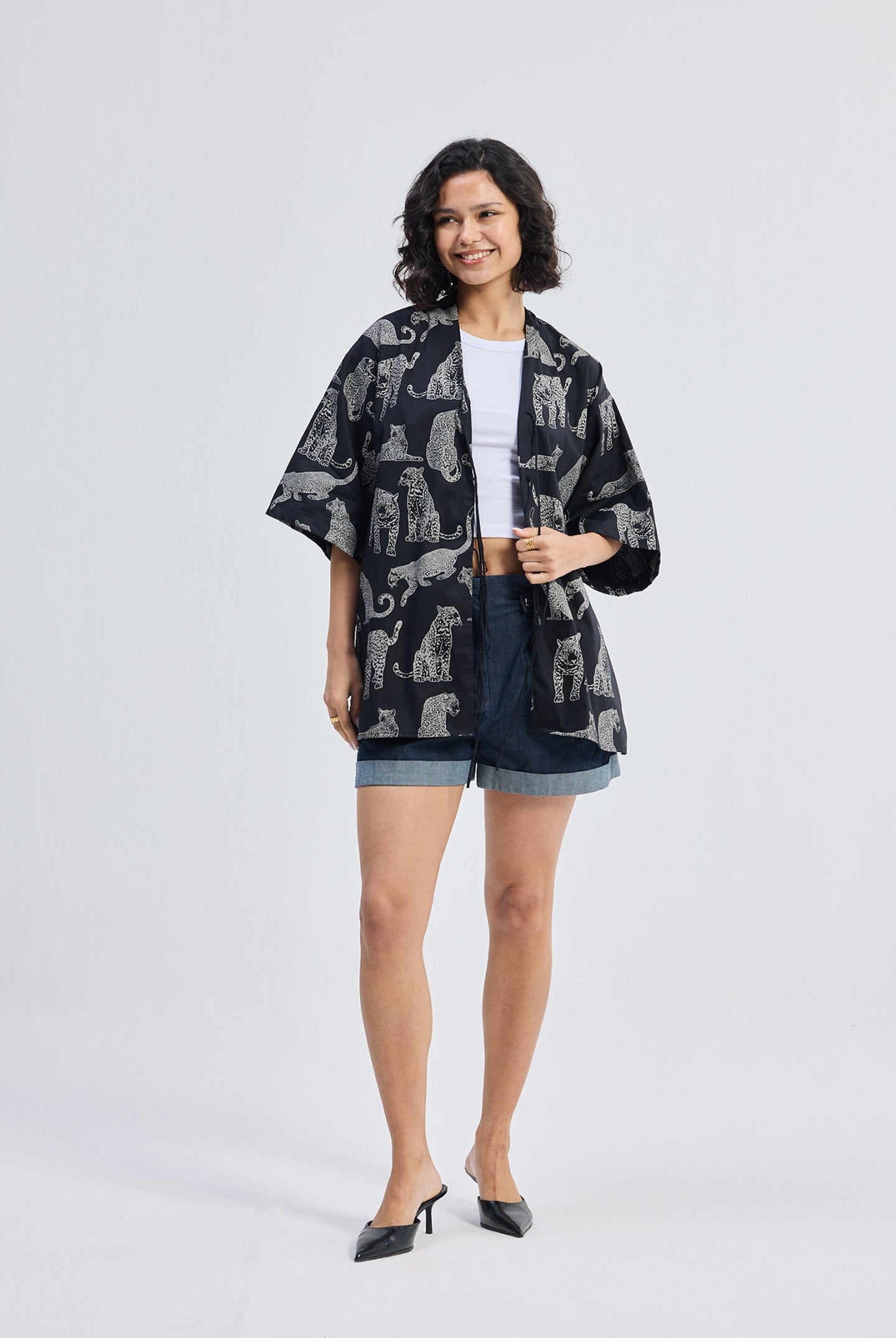 Full-length view of a woman wearing Oversized Shirt with Front-ties in Animal Print by reistor, paired with denim shorts on a white background.