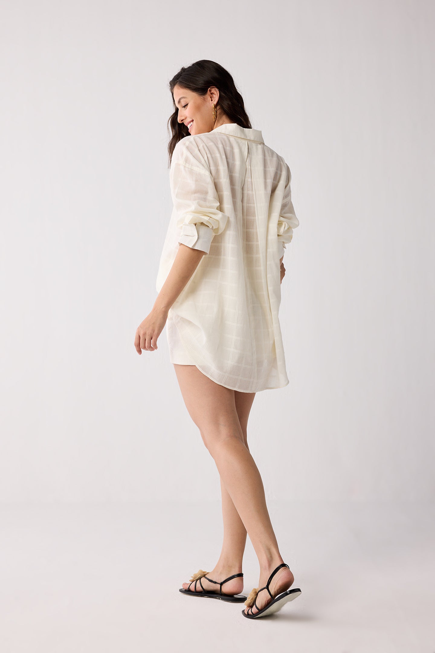 A woman wearing a white shirt and black sandals on a plain background