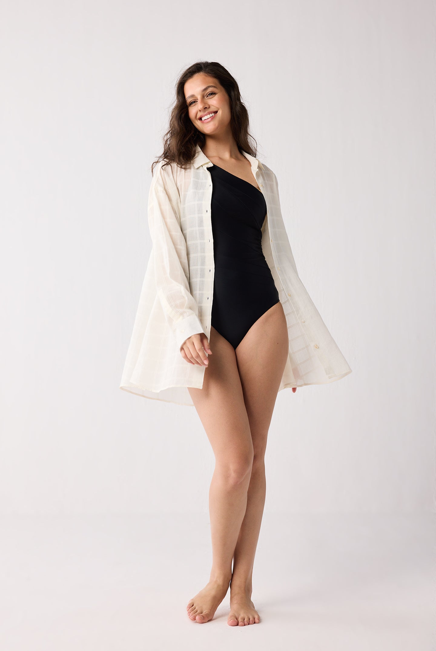 Woman wearing a black swimsuit and white cover-up on a white background