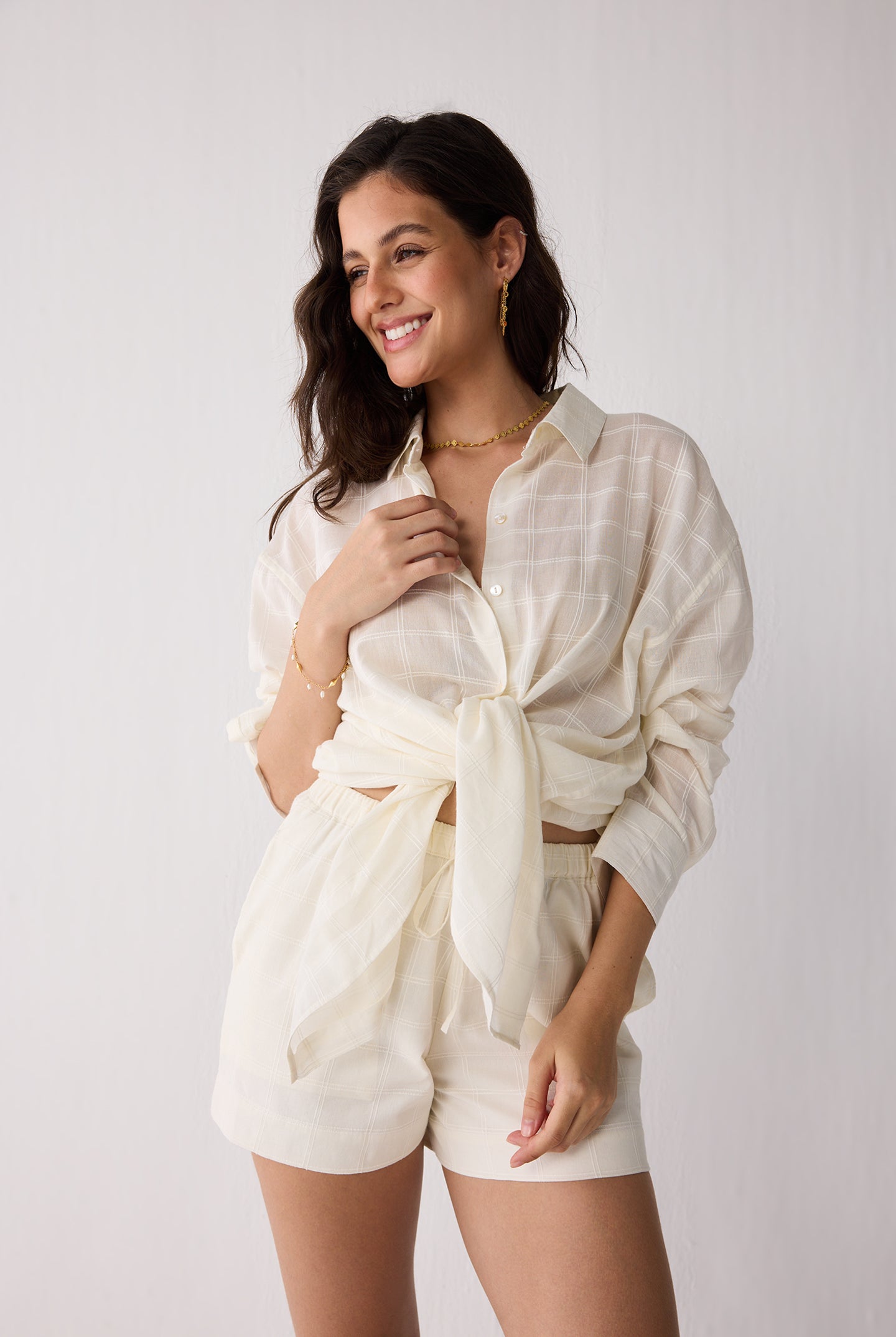 Woman wearing a white outfit with a tied shirt against a plain background