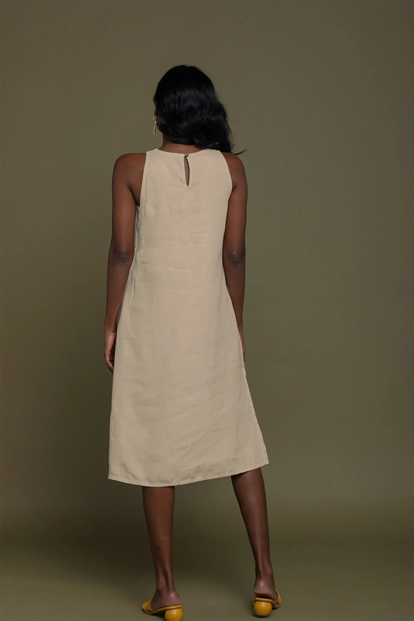 Woman wearing a beige sleeveless dress against a brown background