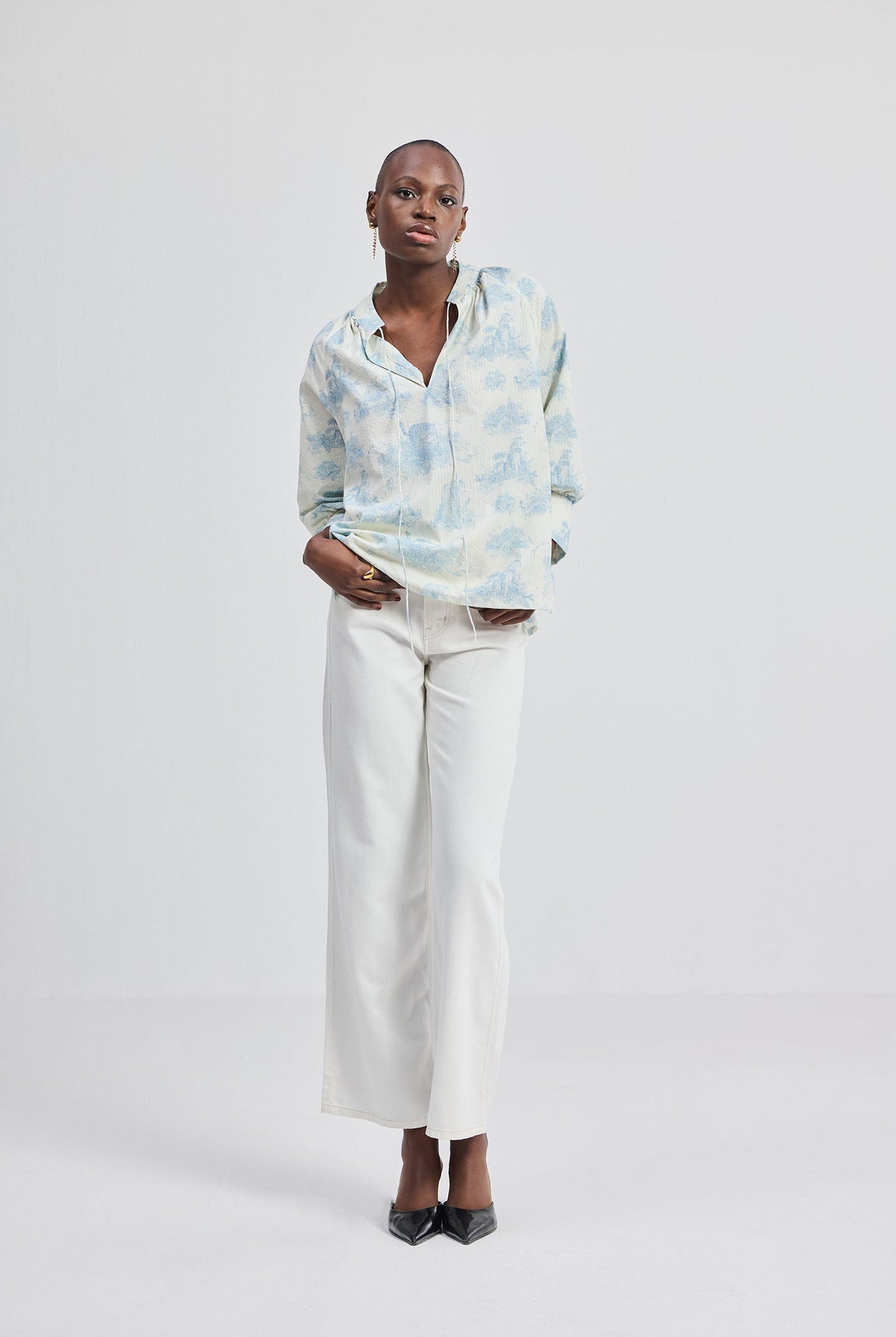 Full-length view of a woman wearing the reistor Relaxed-fit Shirt with Drawstring in Animal Print, styled with white straight-leg pants and heels against a clean studio background.