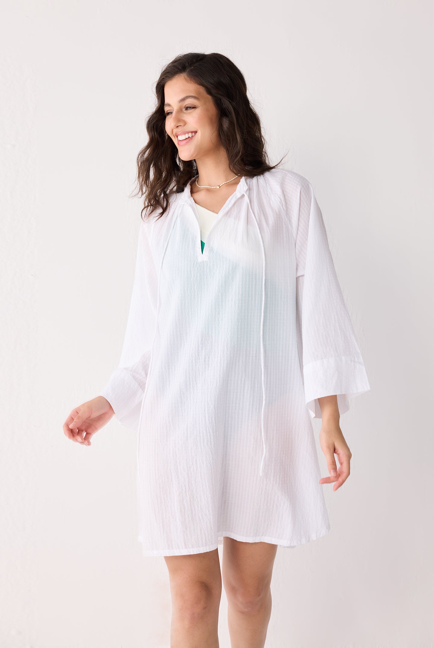 Woman wearing a white striped beach cover-up on a plain background