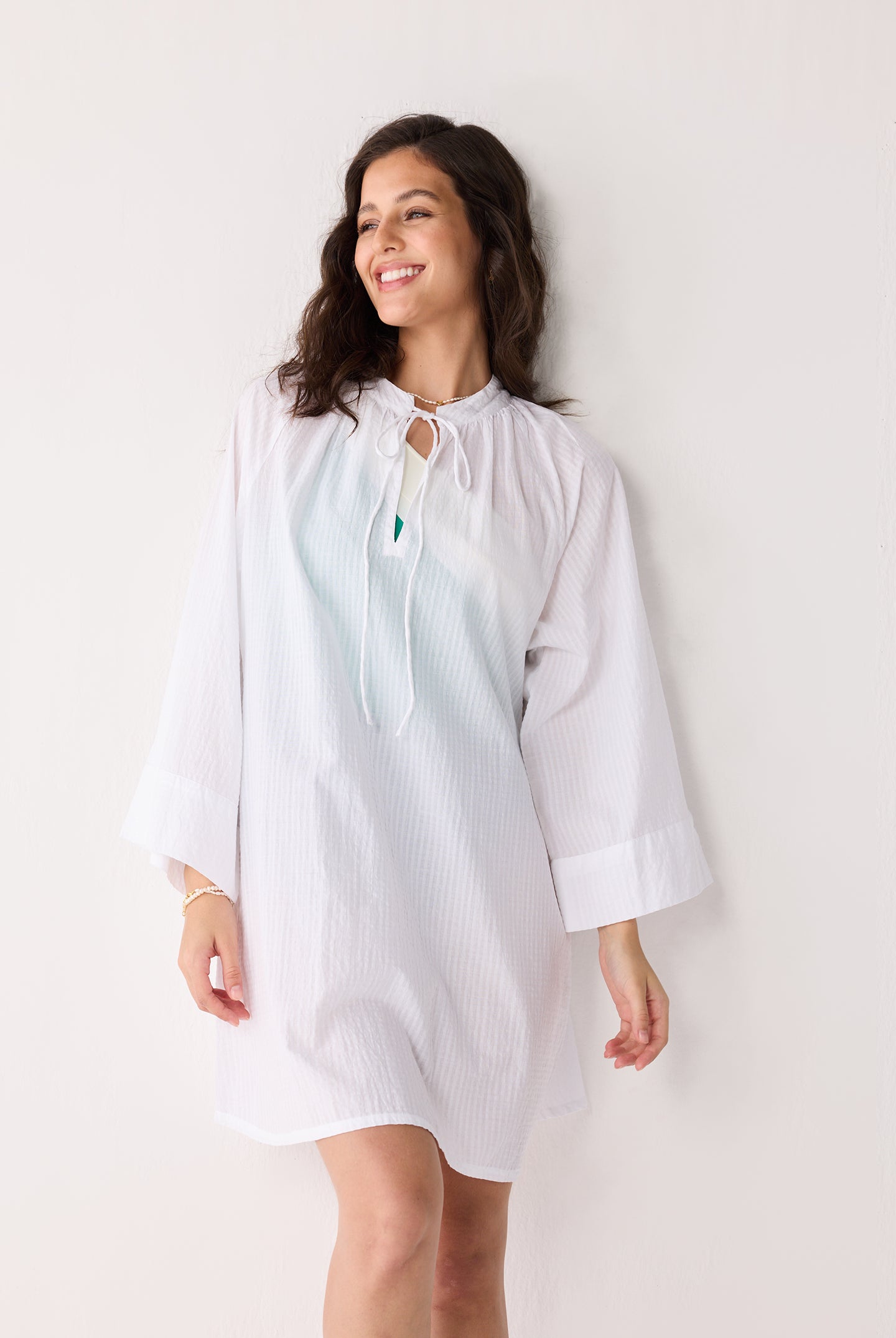 Woman wearing a light-colored cover up with a subtle pattern against a plain background