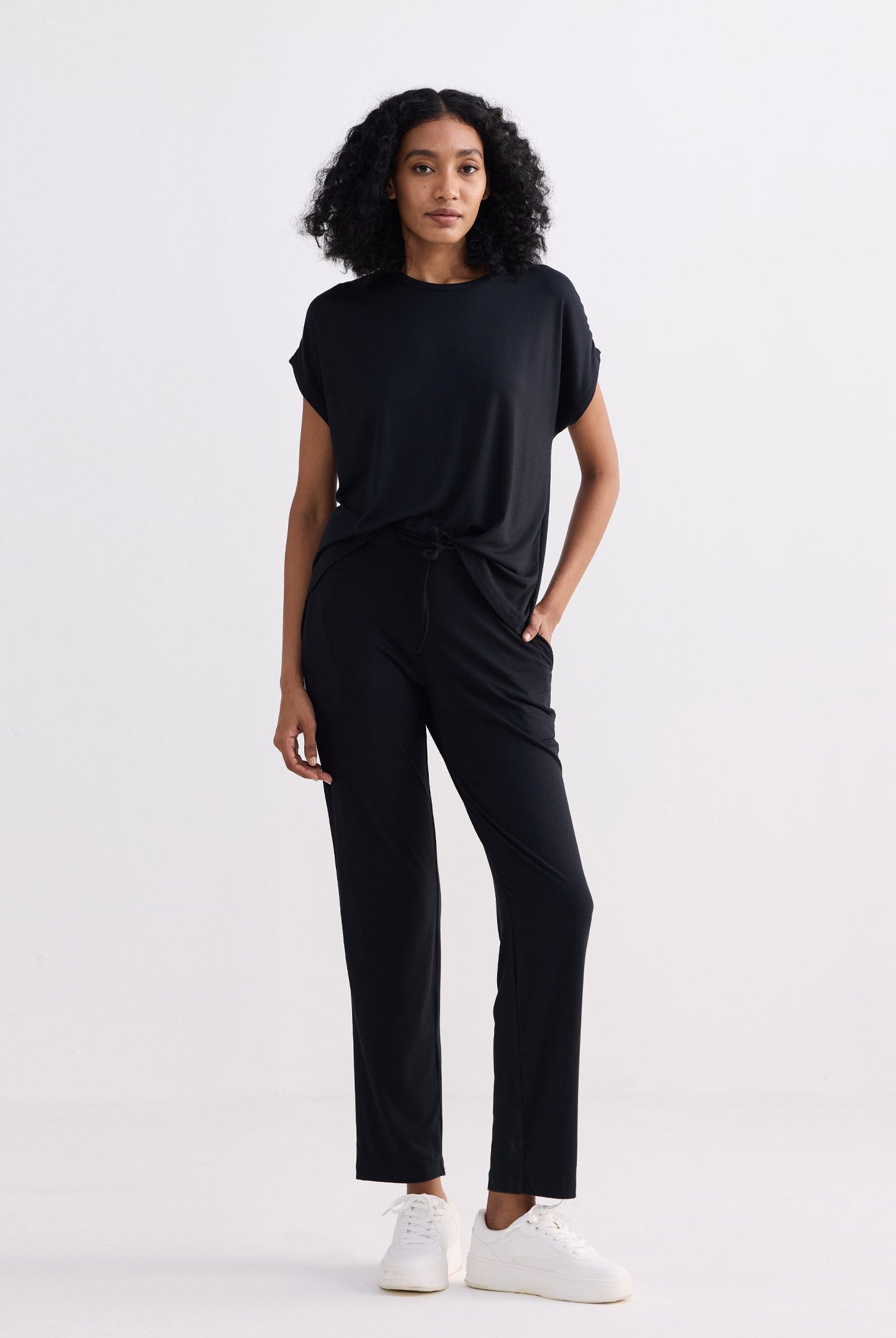 A woman wearing a comfortable black relaxed fit t-shirt and matching pants, standing against a neutral background.