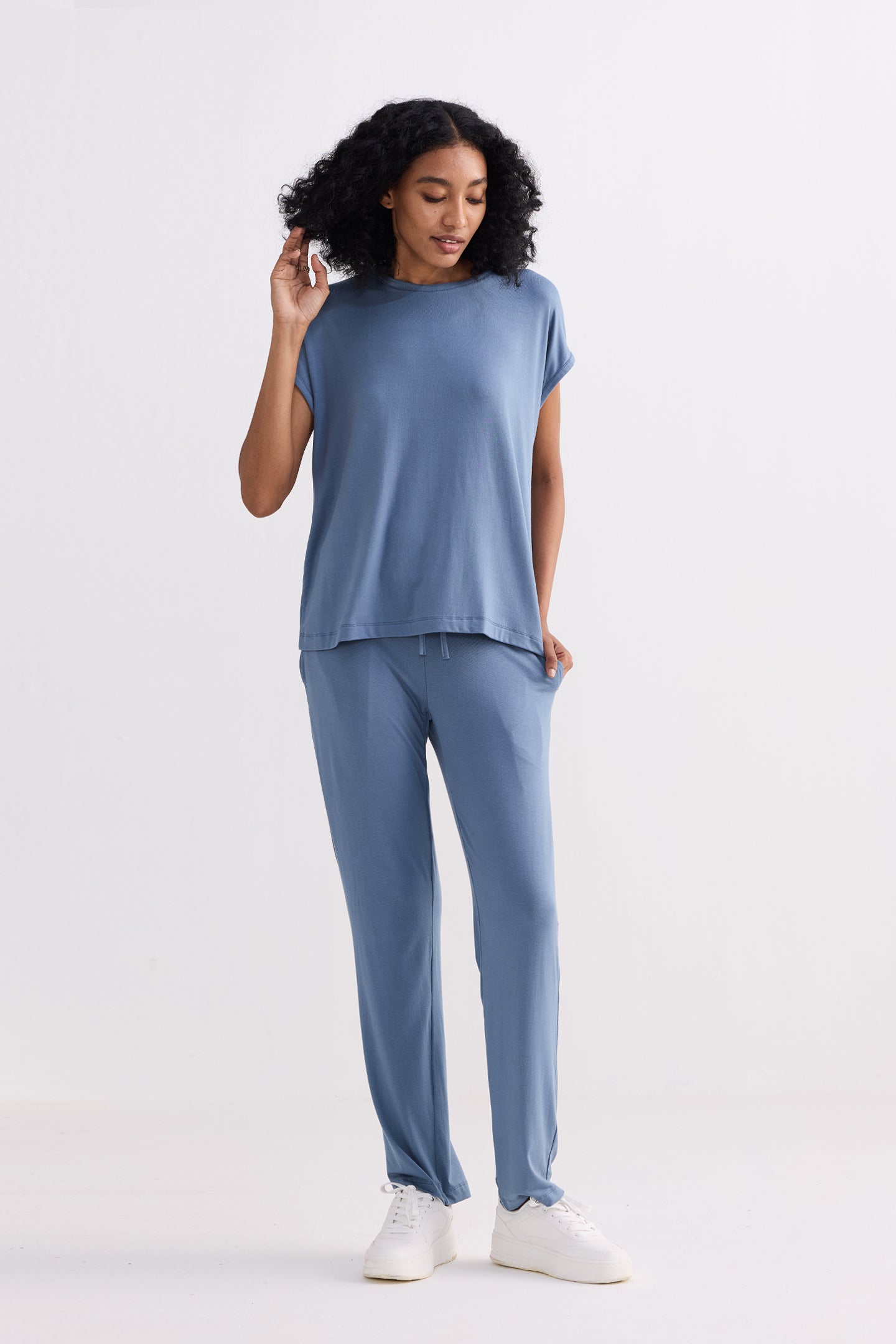 A serene studio portrait of a model showcasing the reistor Relaxed Tee Set in Blue, a minimalist two-piece loungewear ensemble featuring an airy short-sleeve top and fluid, wide-leg drawstring trousers.
