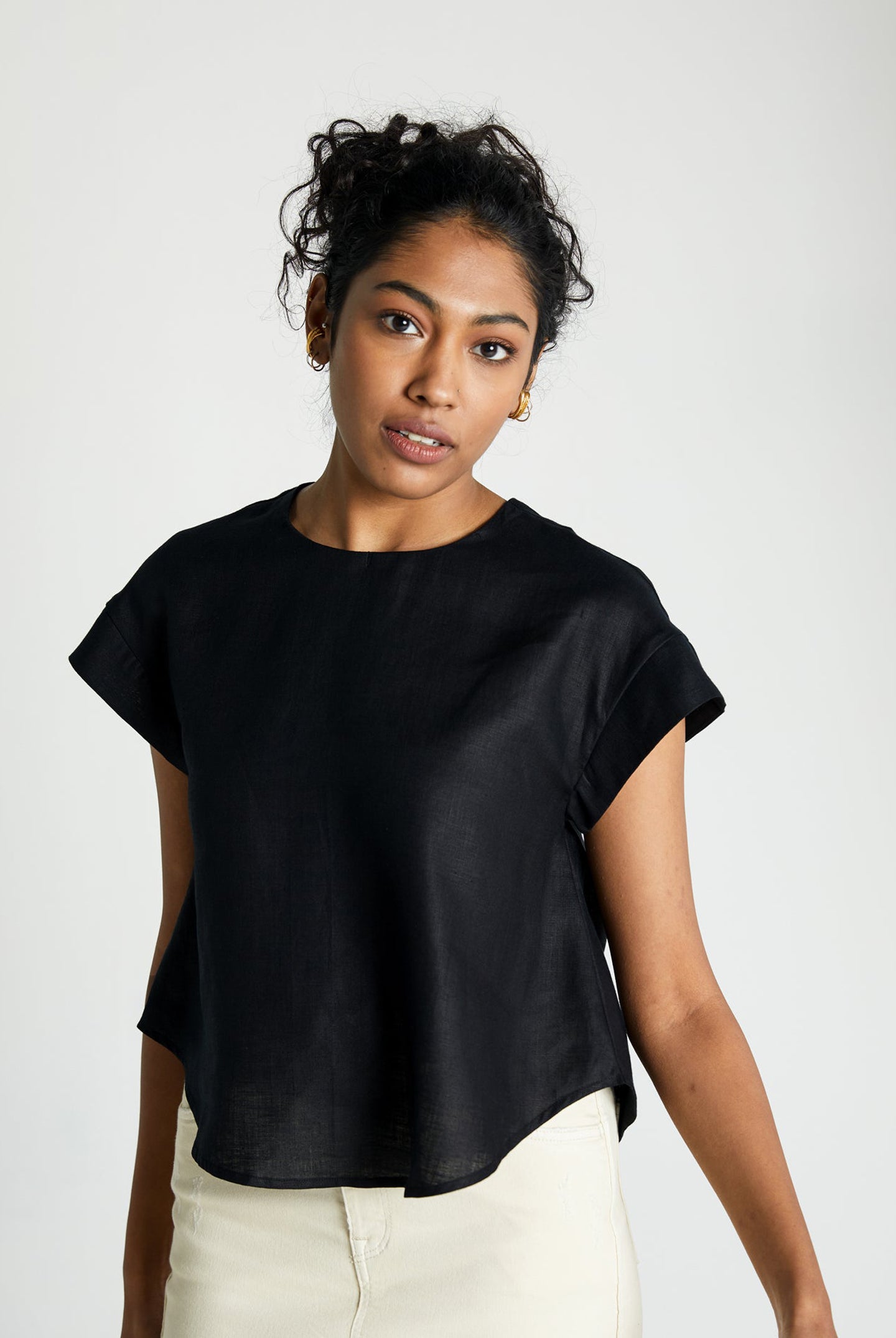 Woman wearing the Reistor Sandcastle Saturdays Top in Black, featuring cap sleeves, a shirttail hem, and a relaxed fit for effortless sustainable everyday style.