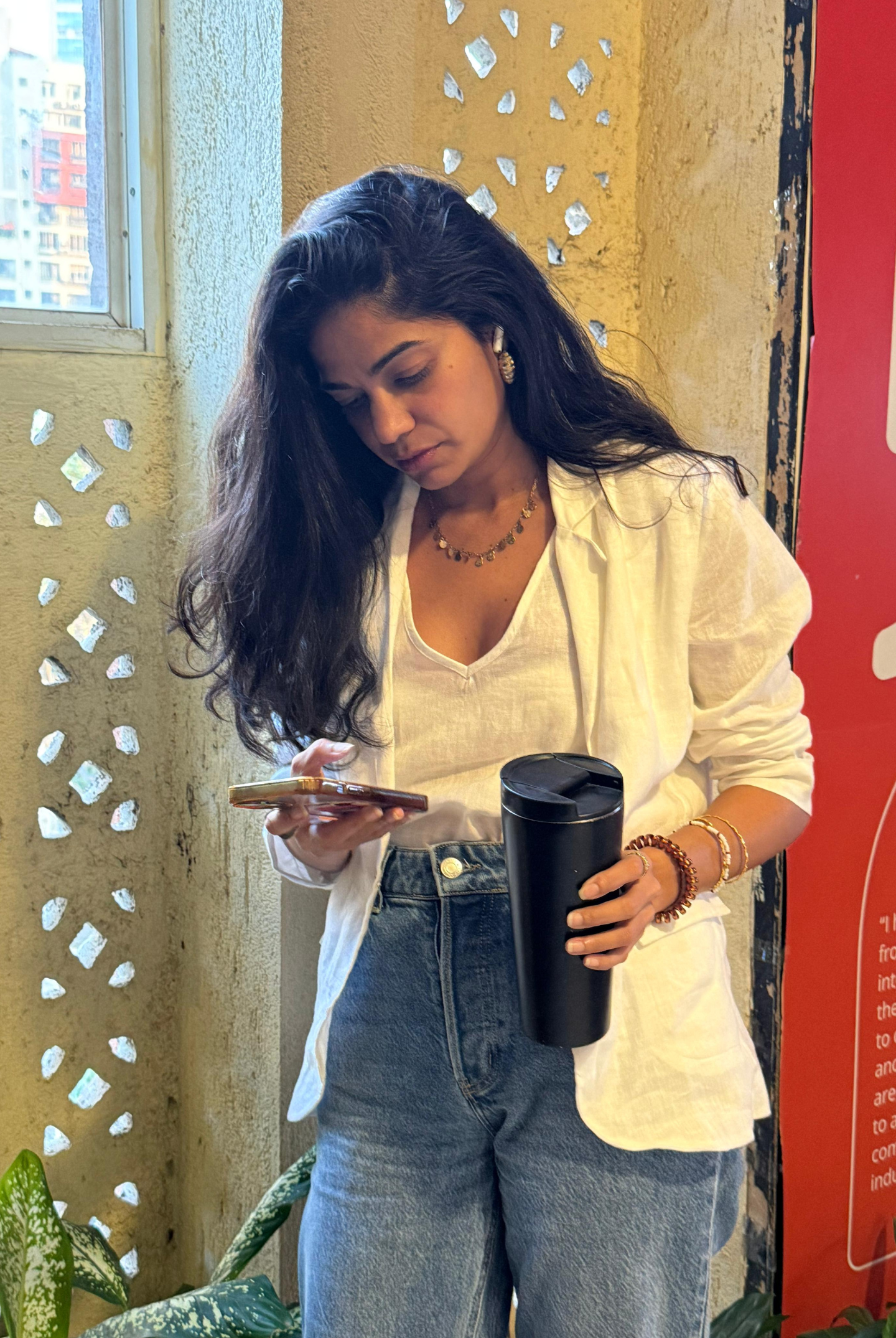 Woman holding a black tumbler and using a phone in an urban setting