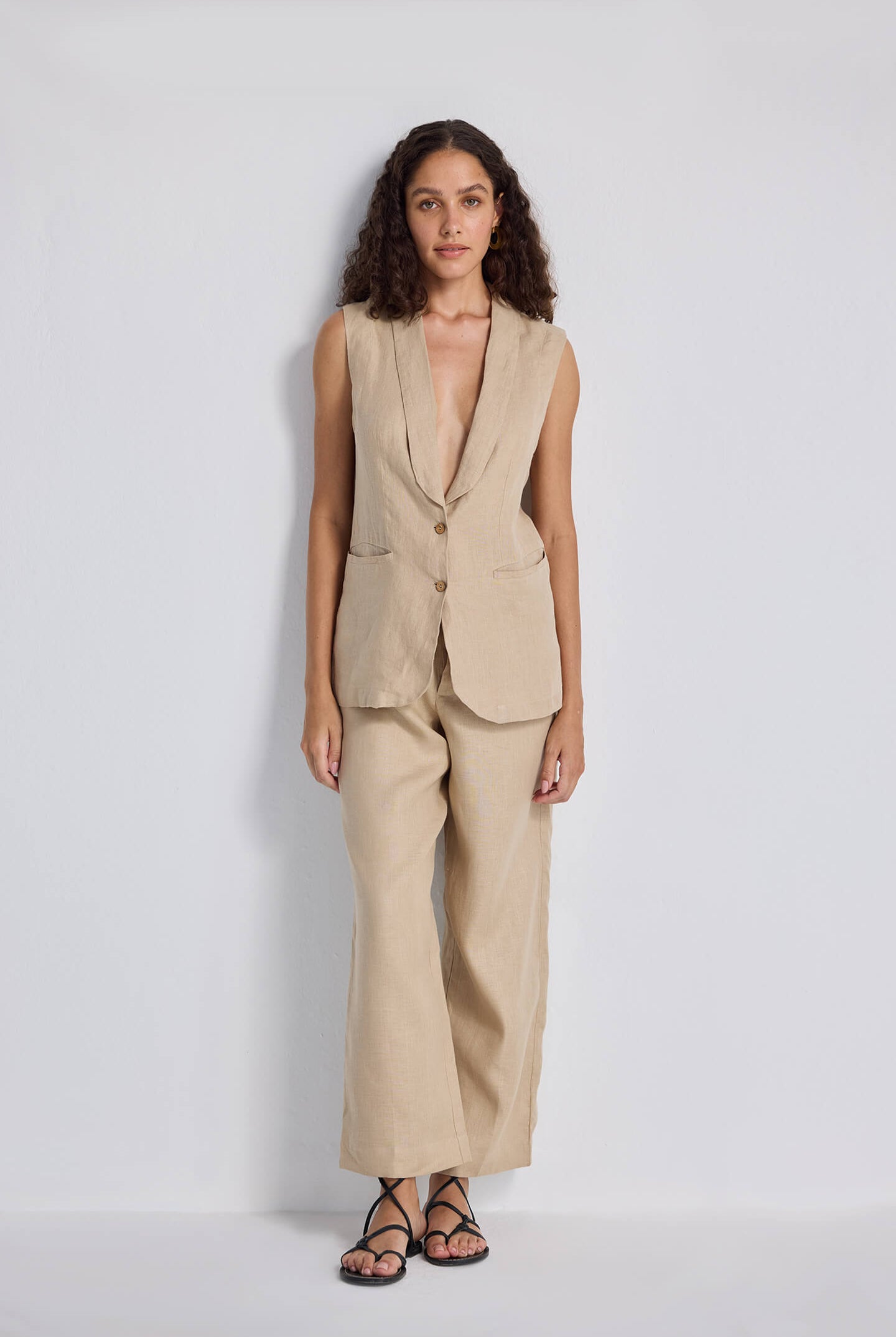 Model wearing the Reistor Sleeveless Hemp Jacket in beige, featuring a tailored fit with front buttons, styled with matching wide-leg pants and sandals.
