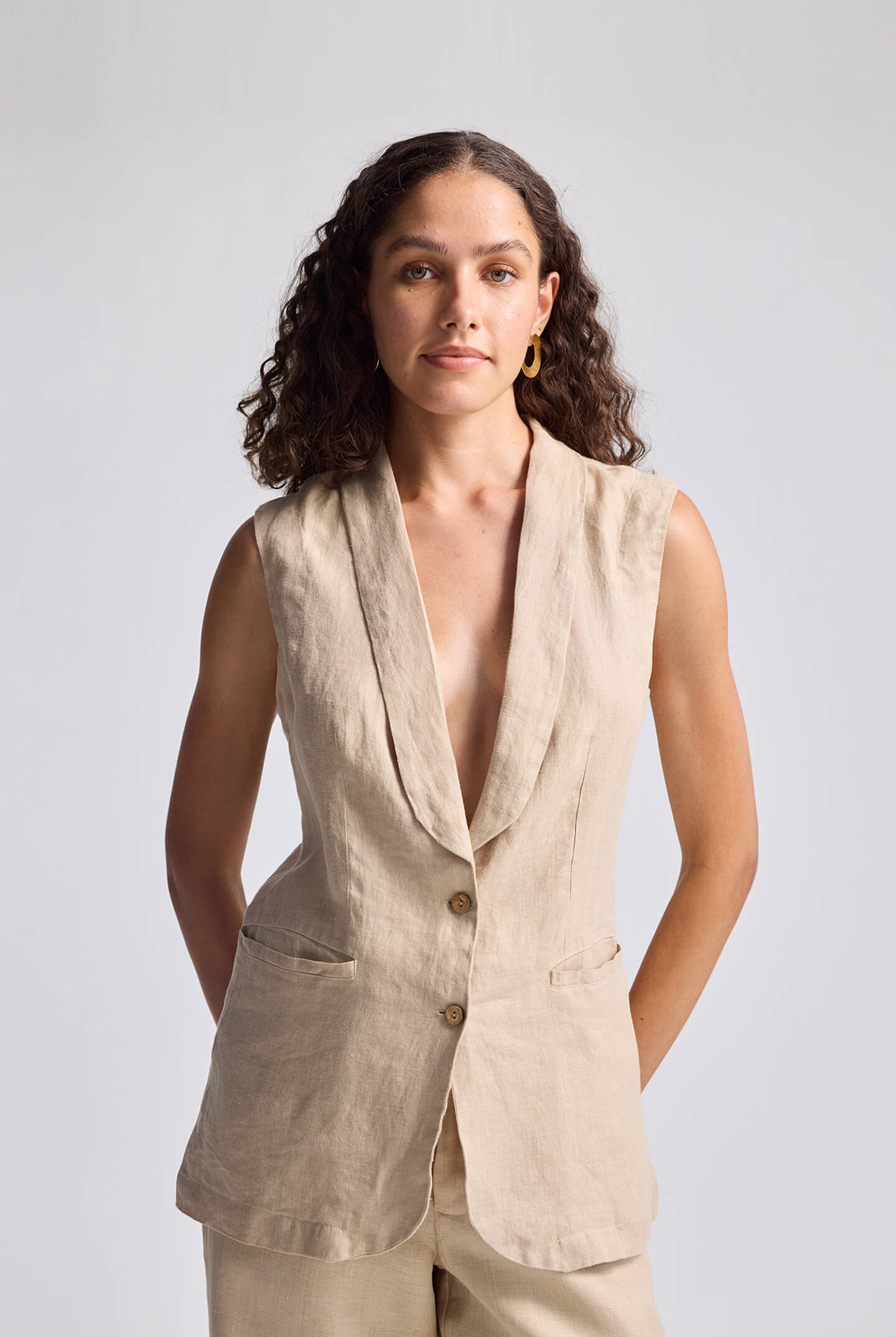 Front view of model wearing Reistor Sleeveless Hemp Jacket in beige, featuring a deep V-neckline, button-front closure, and tailored fit.